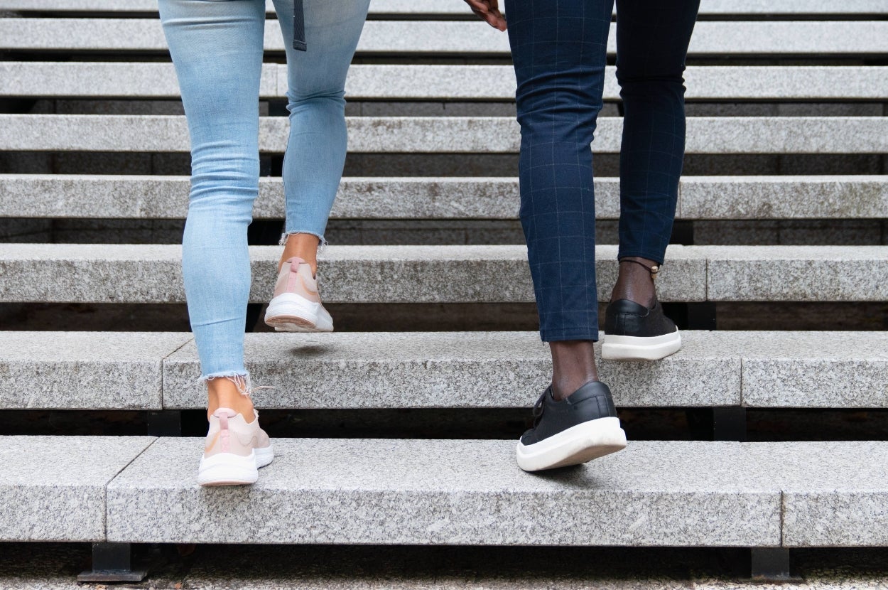 Two people walking up concrete steps, wearing casual jeans and sneakers. Image focuses on their lower legs and feet