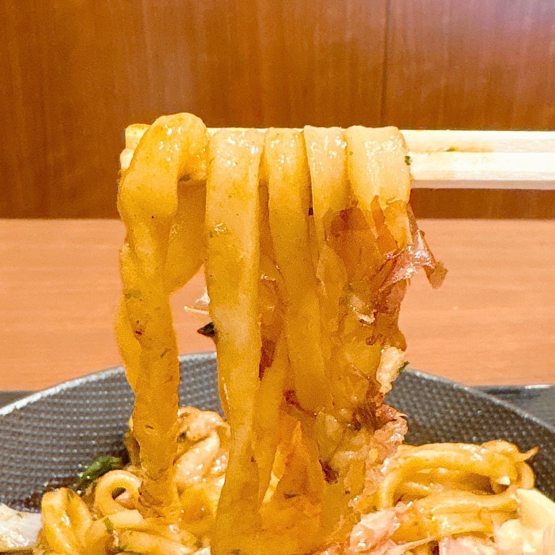 丸亀製麺「丸亀焼きうどん やみつきソース味」のうどんを箸で持ち上げている様子。