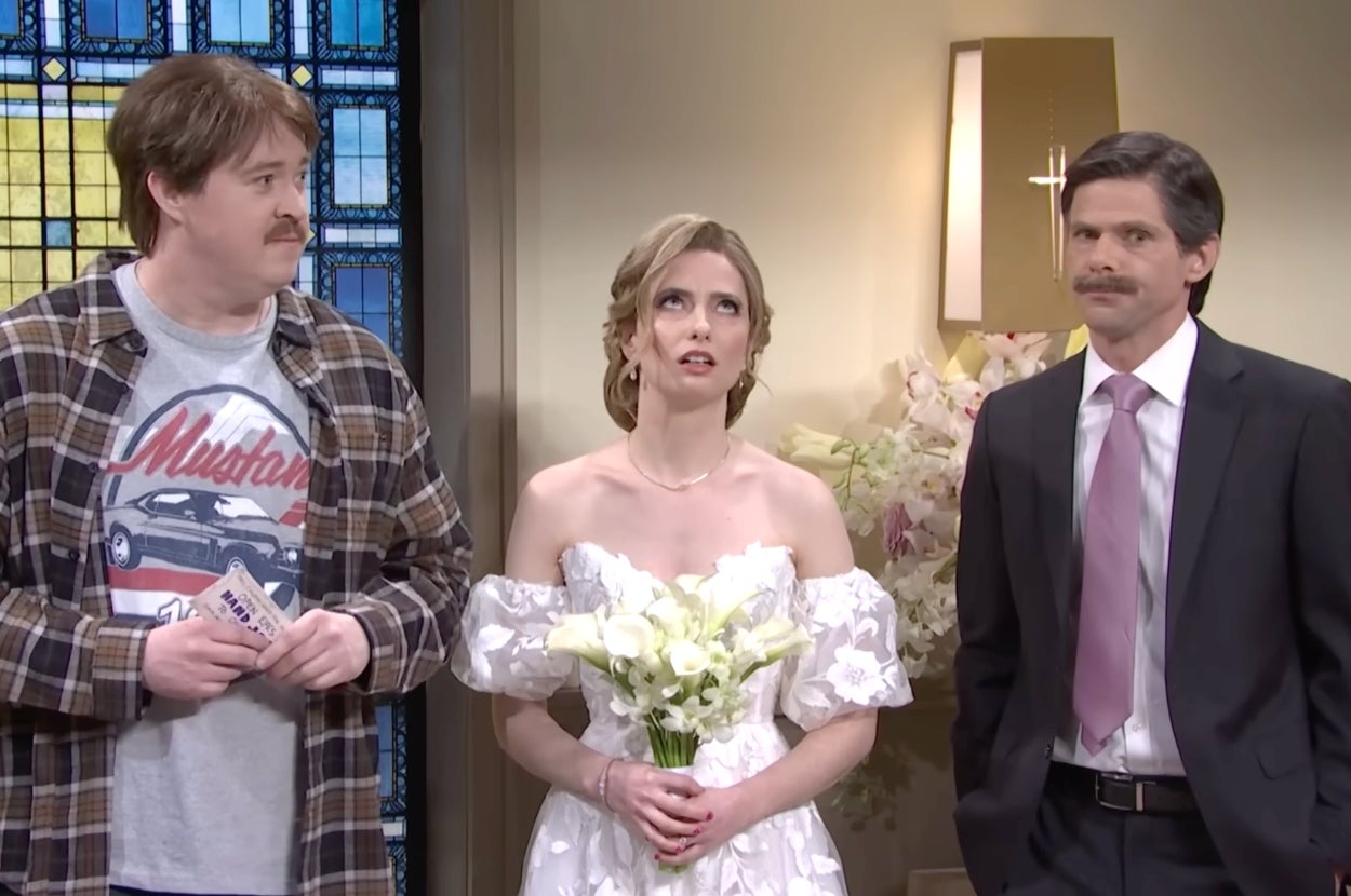 Bride in a white off-shoulder gown holding flowers, standing between two men in suits, one casual with a graphic tee and plaid shirt