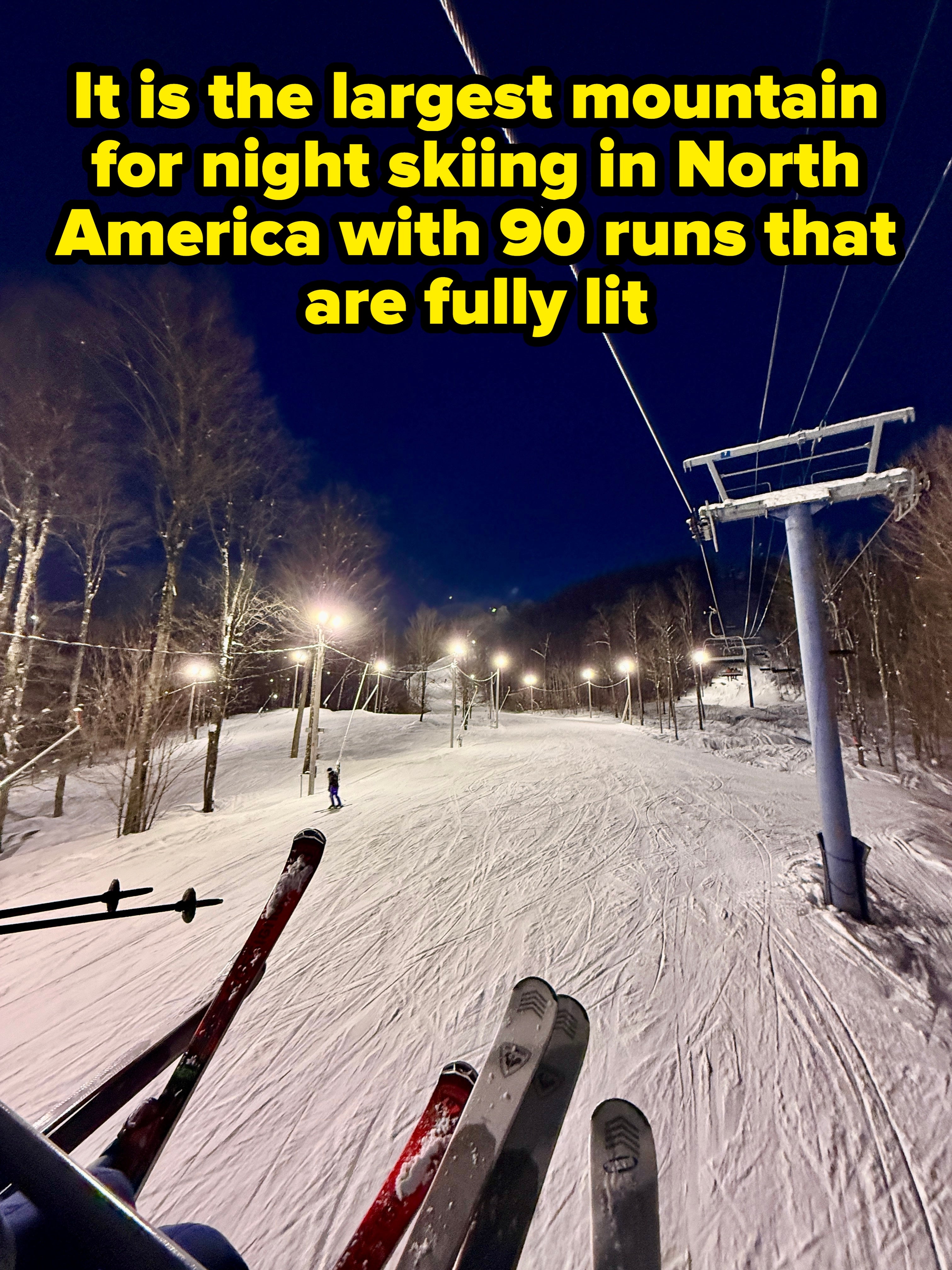 Ski assistance presumption of a snowy slope astatine night, illuminated by lights, with skiers successful the region and trees lining the path