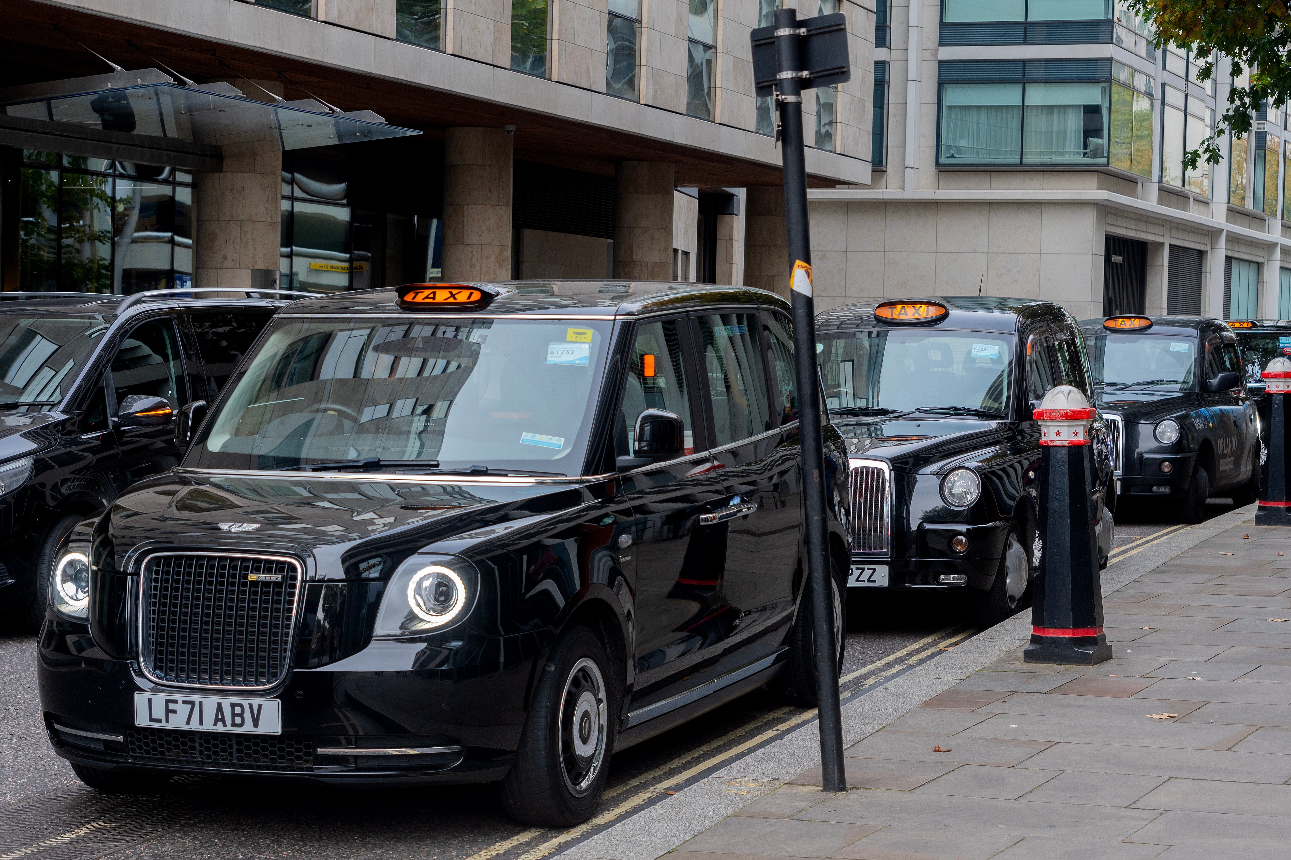 Row of London achromatic taxis parked connected a metropolis thoroughfare adjacent modern buildings, reflecting municipality question and proscription themes