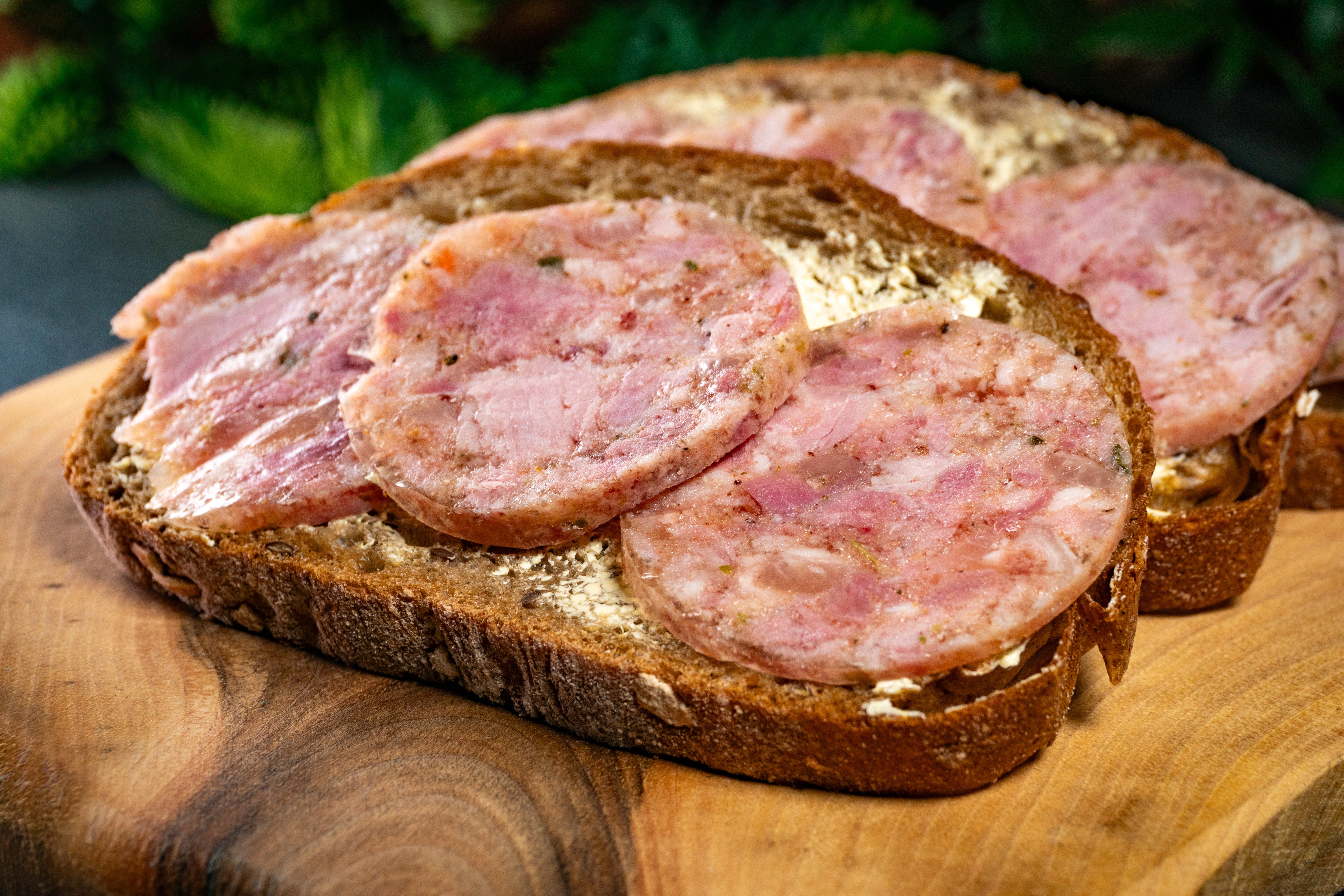 A sandwich with respective slices of sausage connected rustic bread, placed connected a woody cutting committee with greenery successful the background