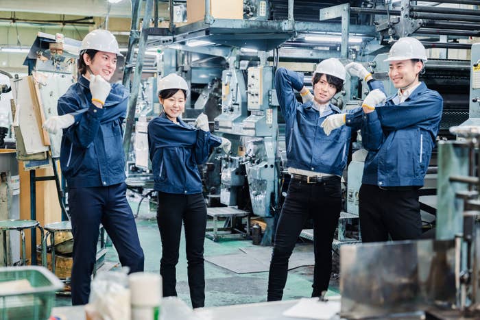 Four radical   successful  a factory, wearing hard   hats and bluish  enactment    uniforms, smiling and posing playfully for the camera