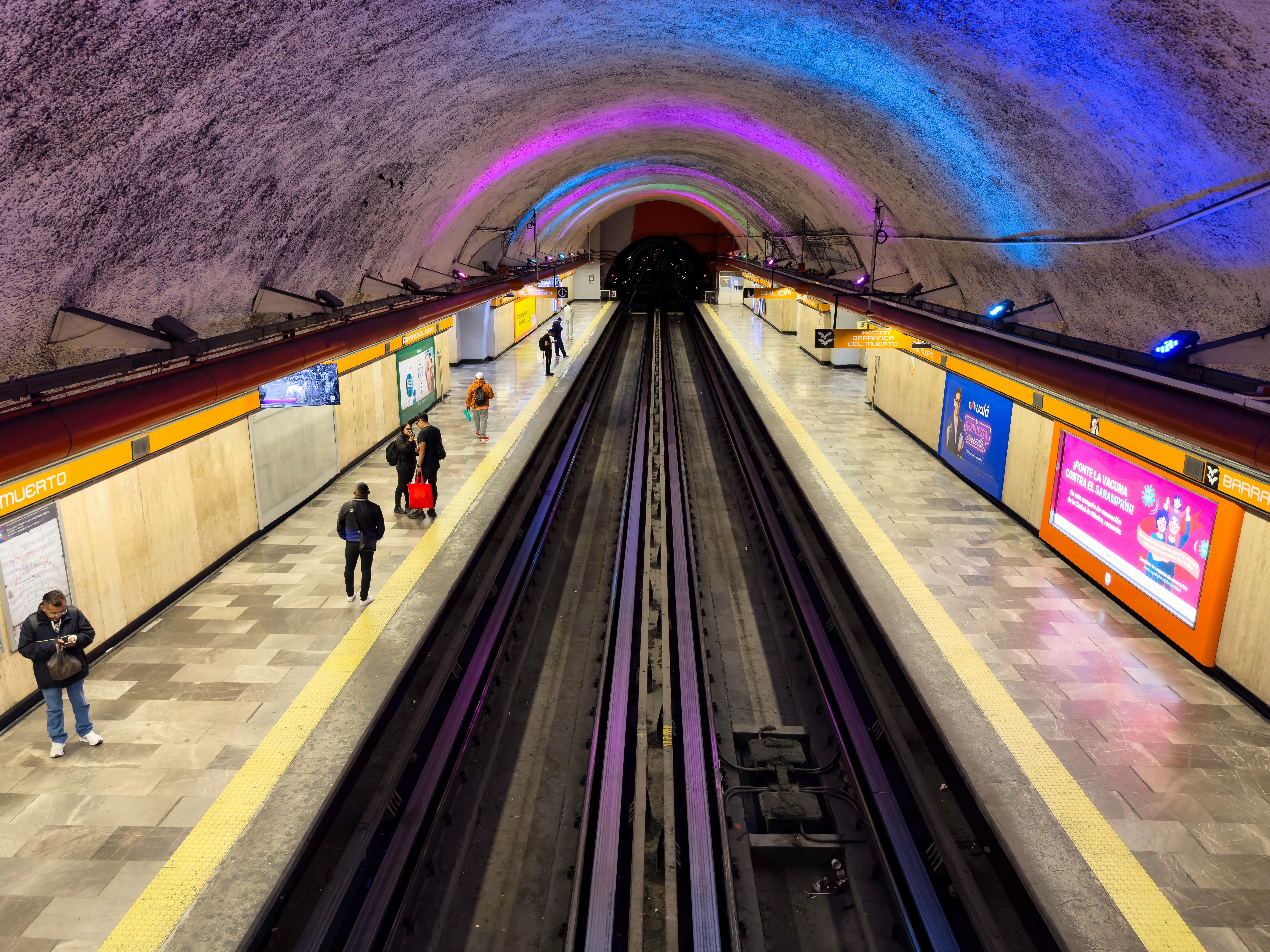 Underground subway presumption with radical walking on the platform, vibrant overhead lighting, and tracks starring into a tunnel