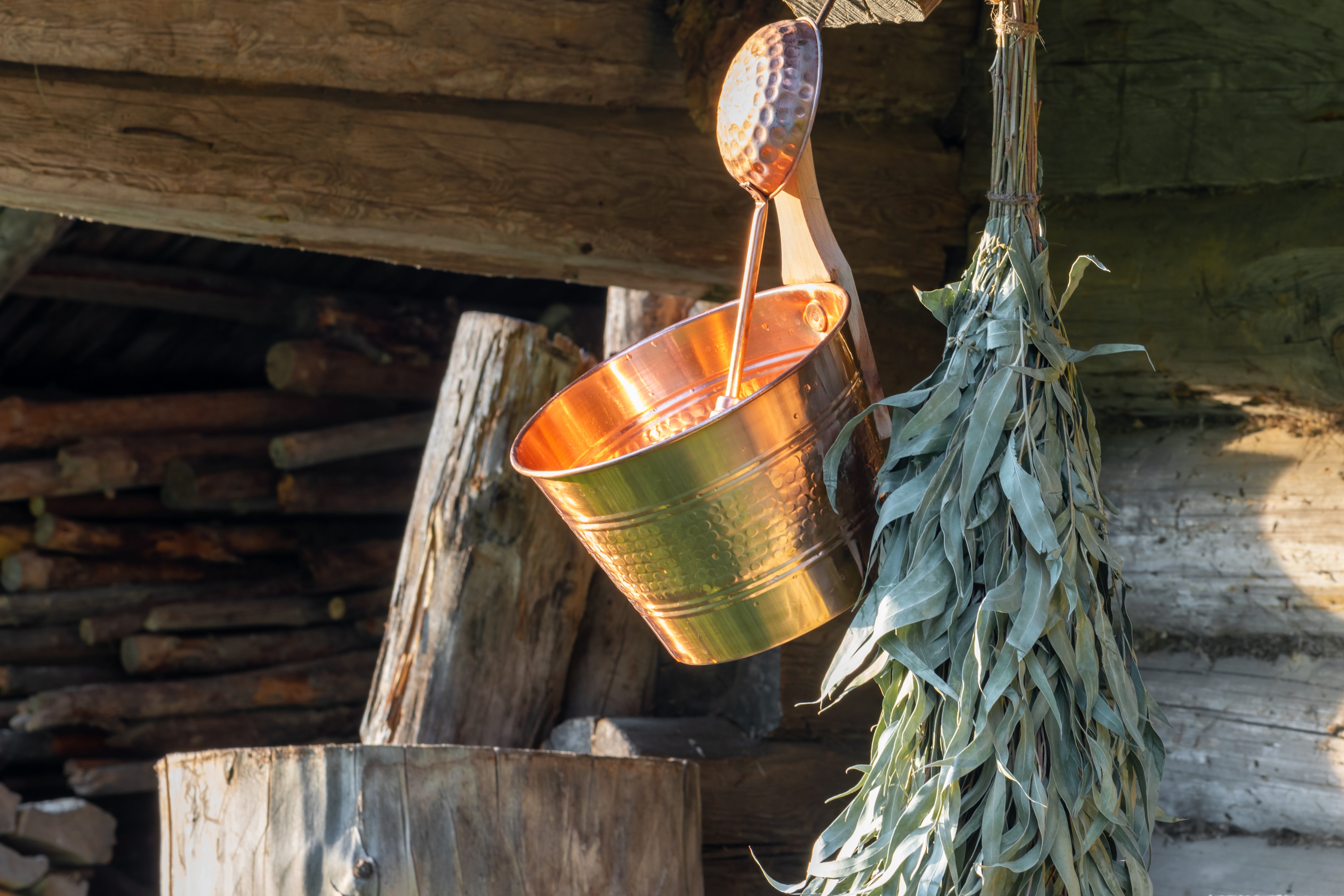Copper bucket and ladle hanging successful a rustic mounting with bundles of herbs nearby, evoking a accepted sauna experience