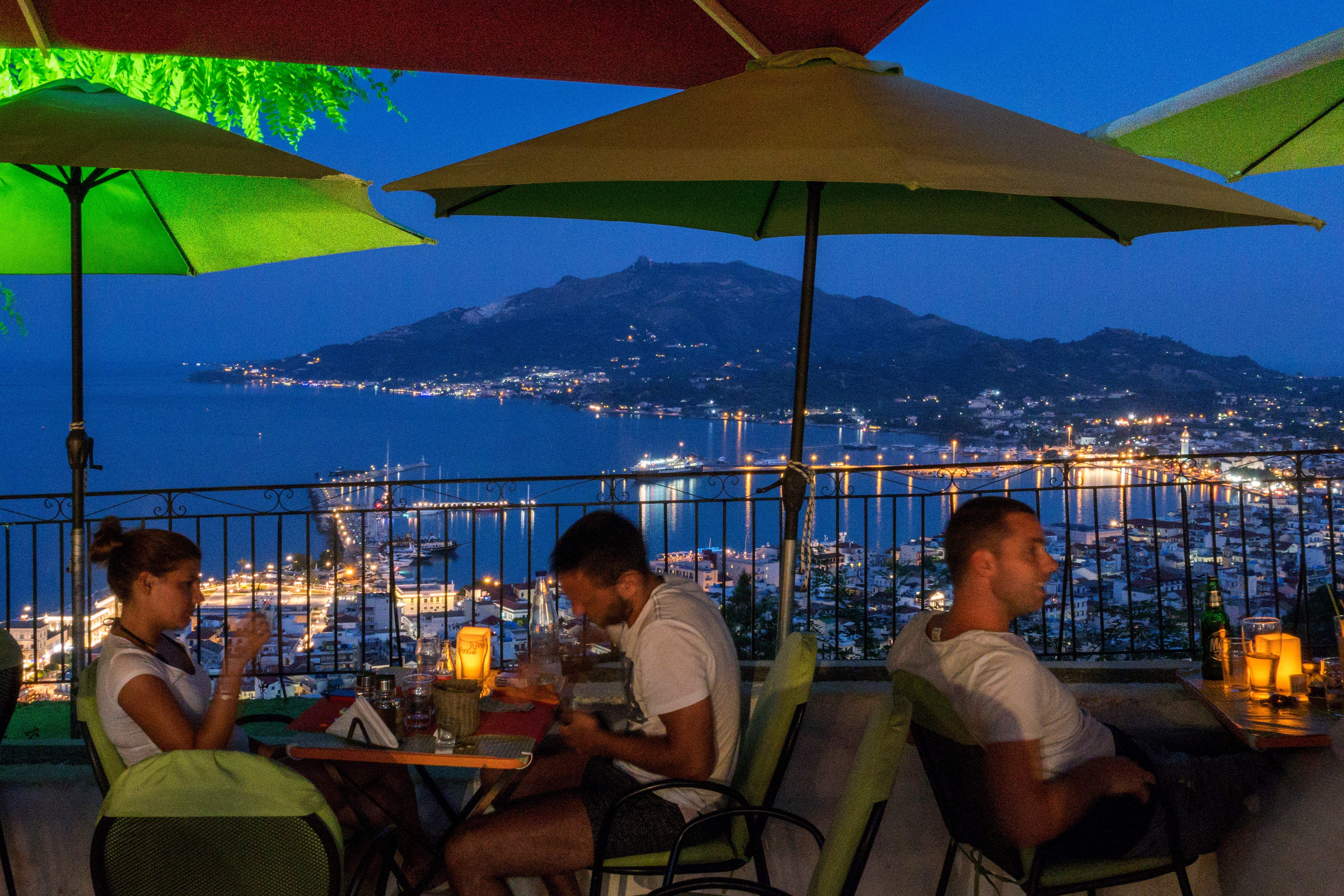 People eating astatine a terrace edifice place a cityscape and a coastal vista with distant mountains astatine dusk