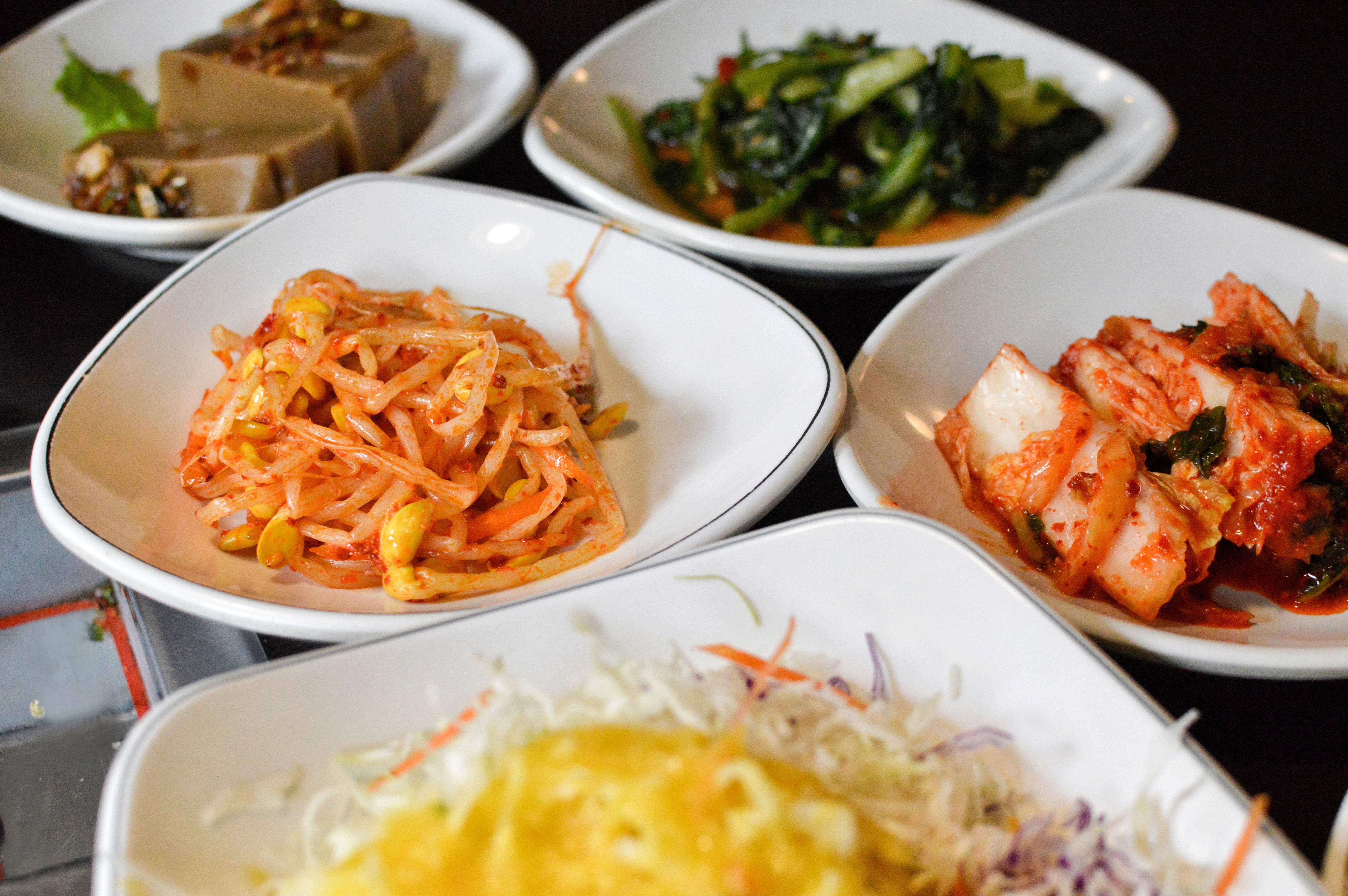 Various Korean broadside dishes, including kimchi and seasoned vegetables, served connected achromatic plates, highlighting divers flavors
