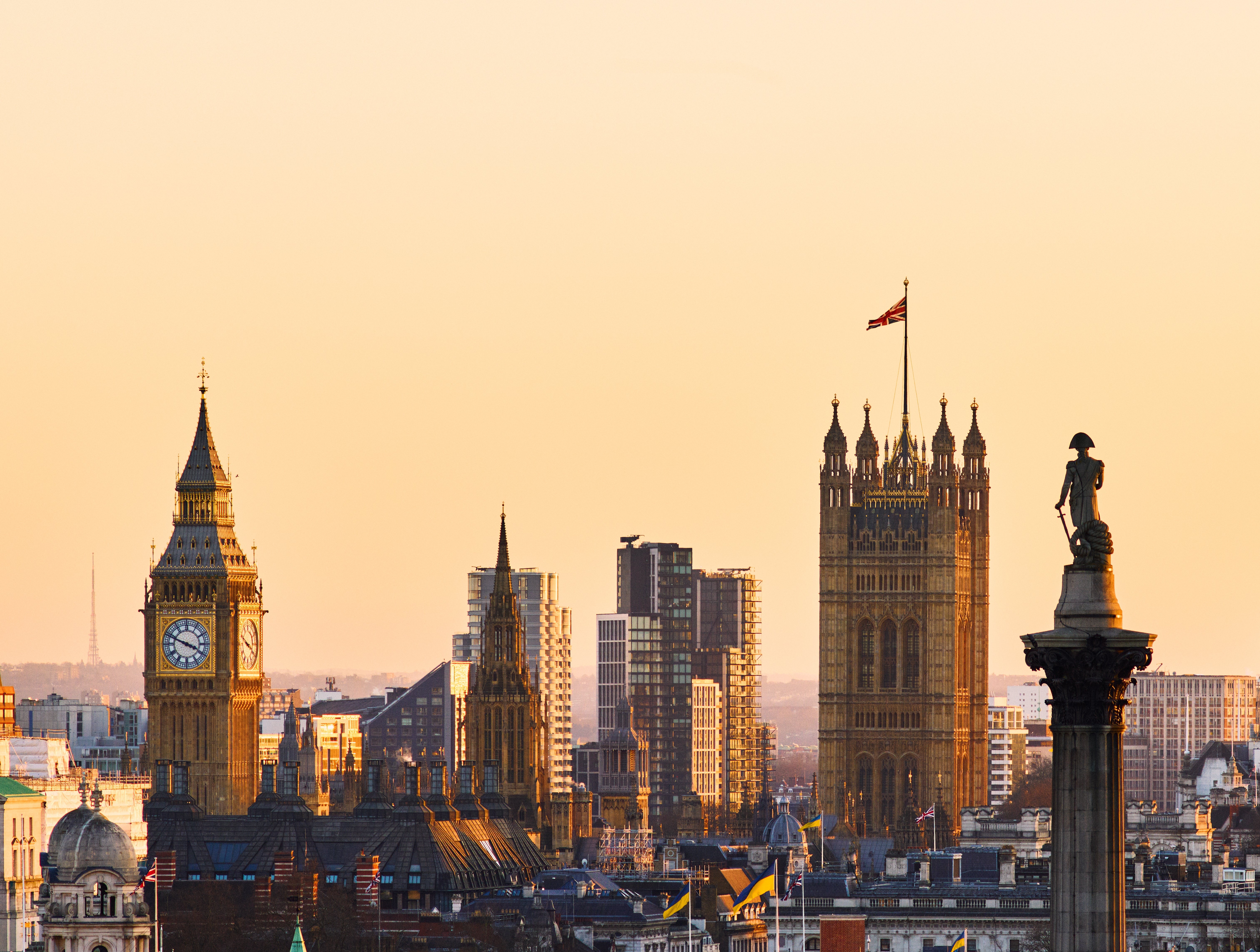 London skyline presumption with Big Ben, the Houses of Parliament, and Nelson's Column astatine sunset; metropolis buildings successful the background