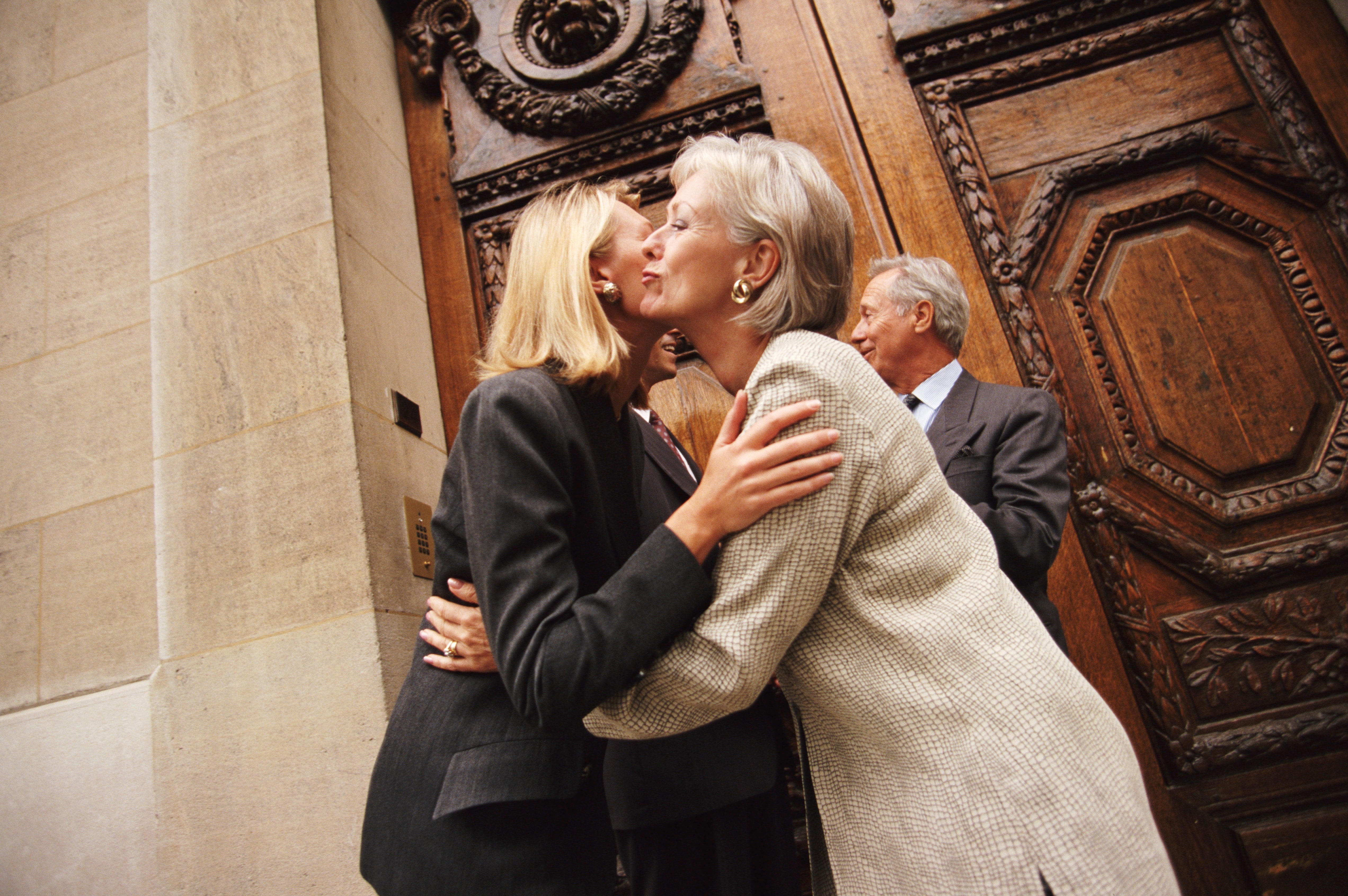 People greeting each different with feature kisses extracurricular a large, ornate door, suggesting a societal gathering oregon question event