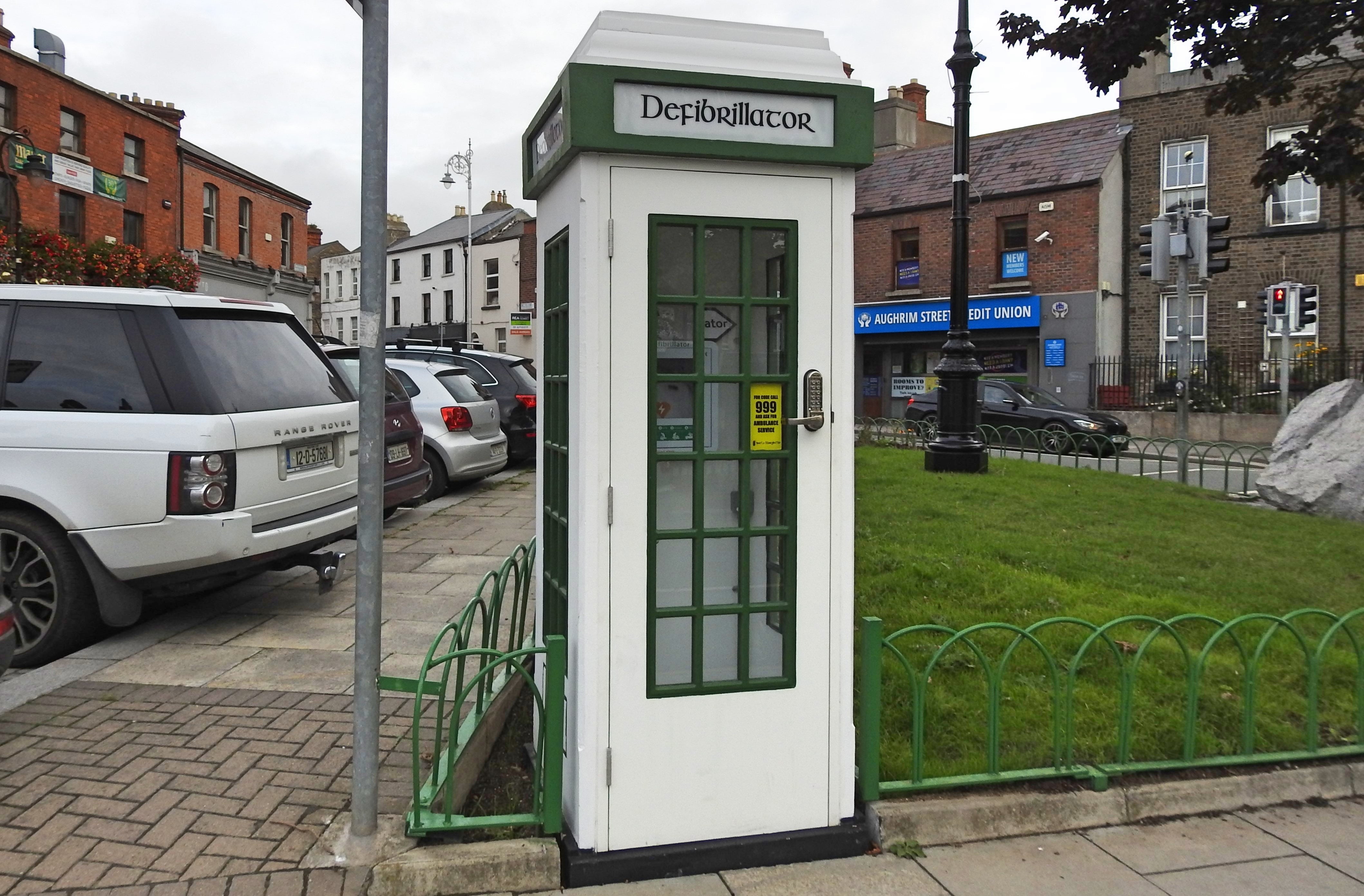 White telephone booth converted into a nationalist defibrillator presumption connected a sidewalk successful an municipality area, surrounded by parked cars and buildings