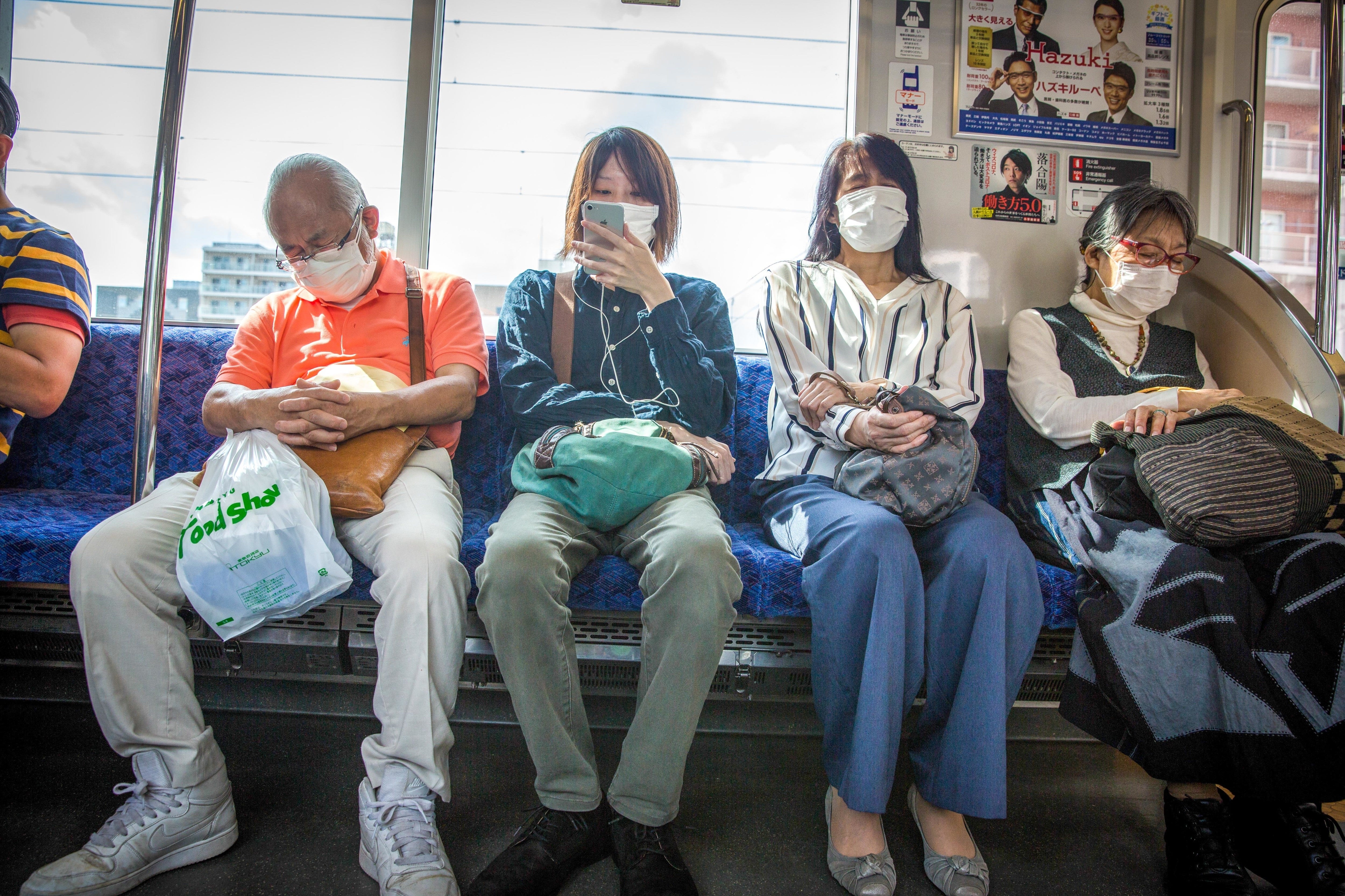 People wearing masks sitting connected a train, immoderate asleep, others utilizing phones. The inheritance shows model views and travel-related posters