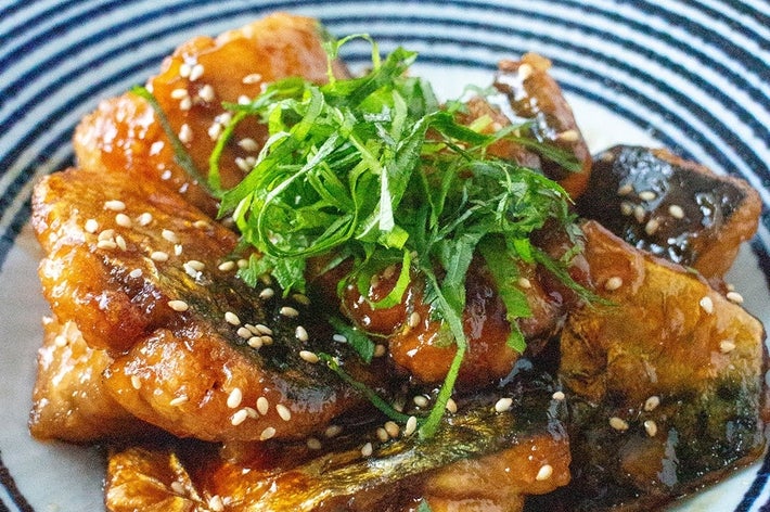 皿に盛られたタレで煮た魚とゴマ、緑の葉が添えられた料理。