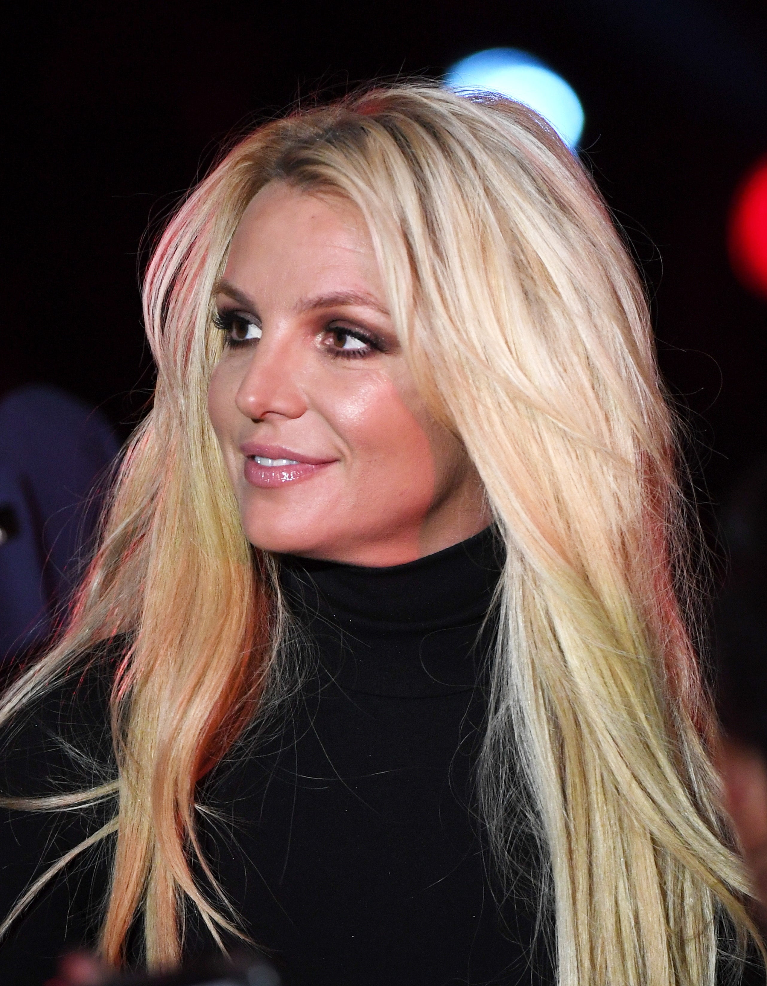 Person with long, styled hairsbreadth and a achromatic turtleneck, smiling portion looking sideways