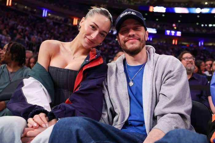 Two radical   sitting unneurotic  astatine  an event, smiling. One wears a casual overgarment   implicit    a conduit  top; the different   wears a airy  overgarment   implicit    a bluish  shirt