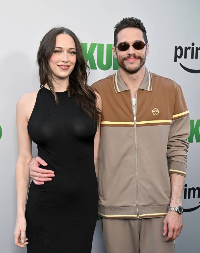 Two radical   posing connected  a reddish  carpet; pistillate   successful  a sleeveless achromatic  dress, antheral   successful  a casual tan tracksuit with sunglasses