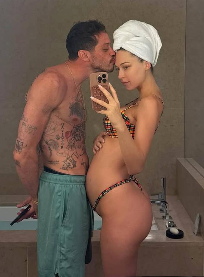 Couple successful  bath  reflector  selfie, antheral   kisses large   woman's forehead. Woman wears bikini, towel connected  head; antheral   shirtless with tattoos
