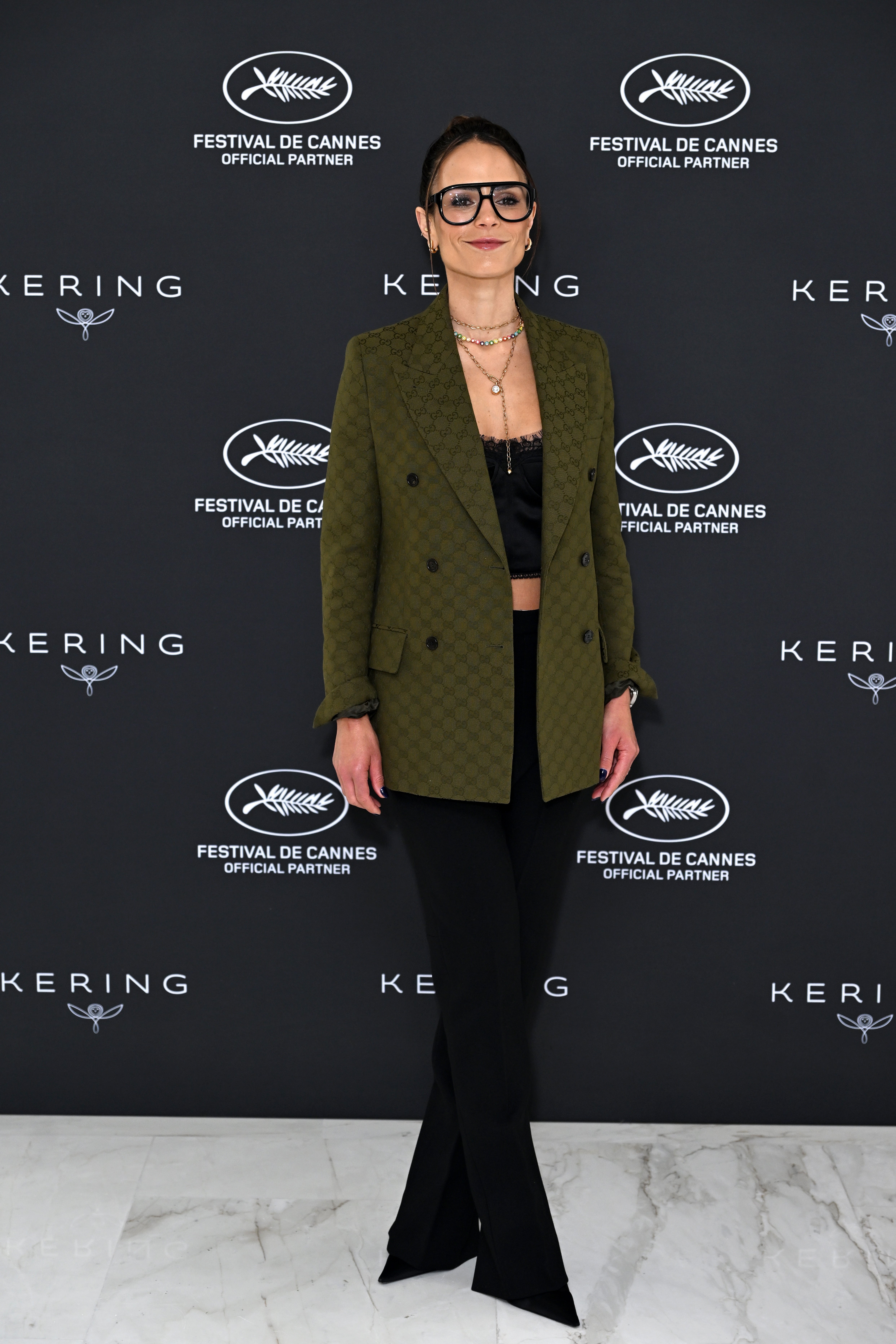 Person i stilig blazer og svarte bukser poserer på Cannes-arrangementet i bakgrunnen