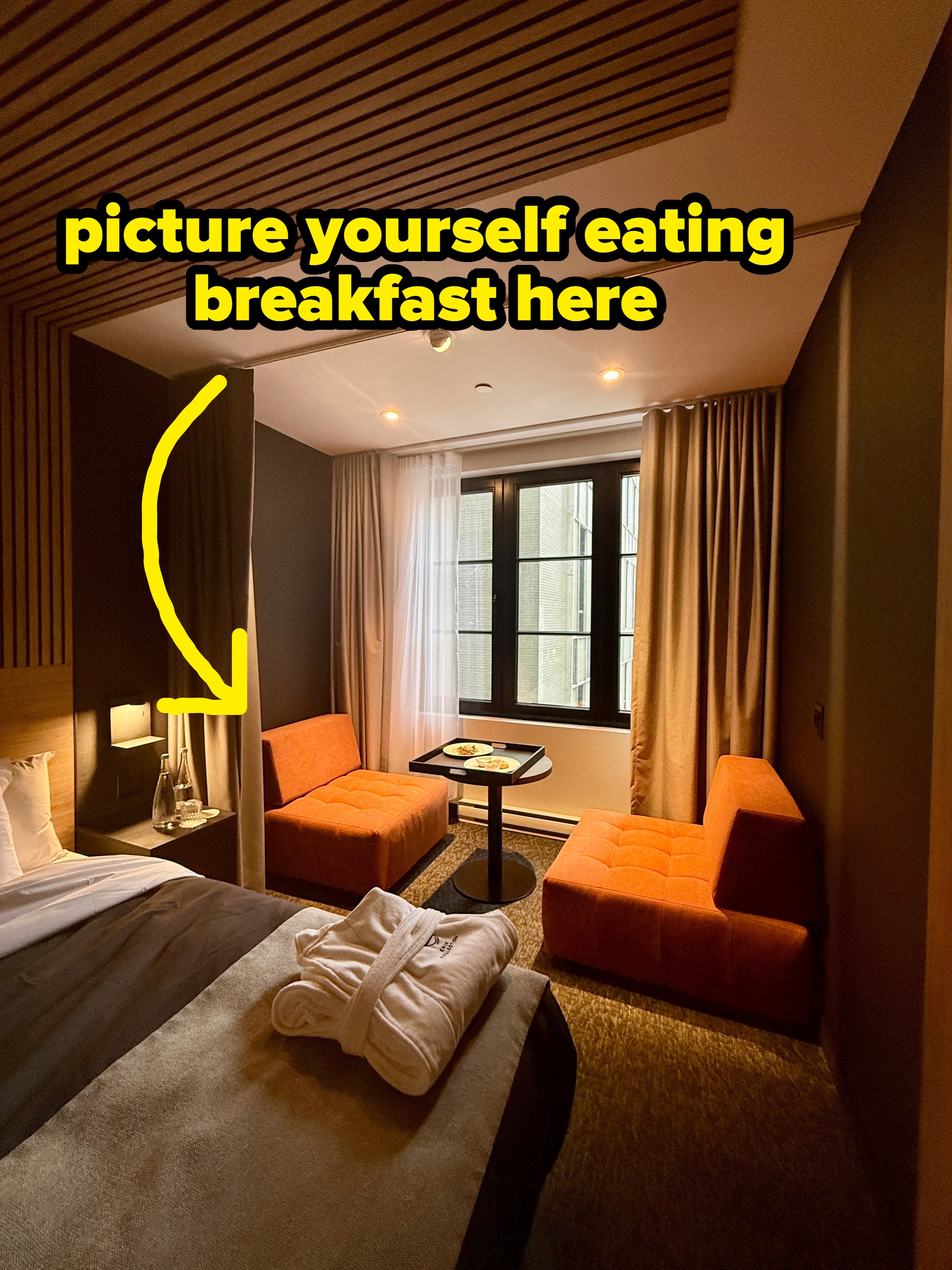 Cozy edifice country with a bed, 2 orangish chairs, a tiny table, and a ample model with drawn curtains