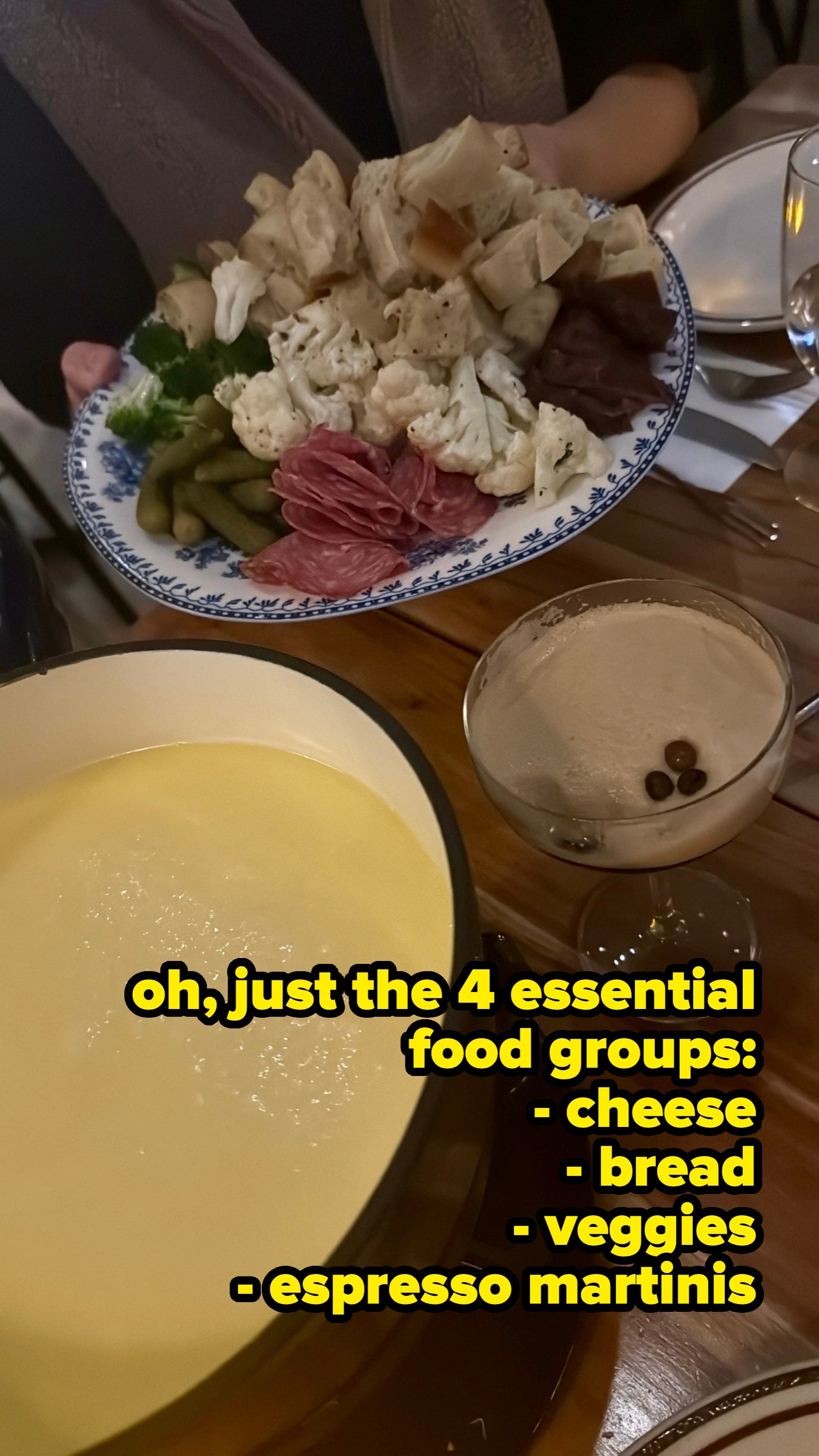 Fondue cookware with melted cheese, a platter of meats and vegetables, and a cocktail connected a woody array successful a cozy eating setting