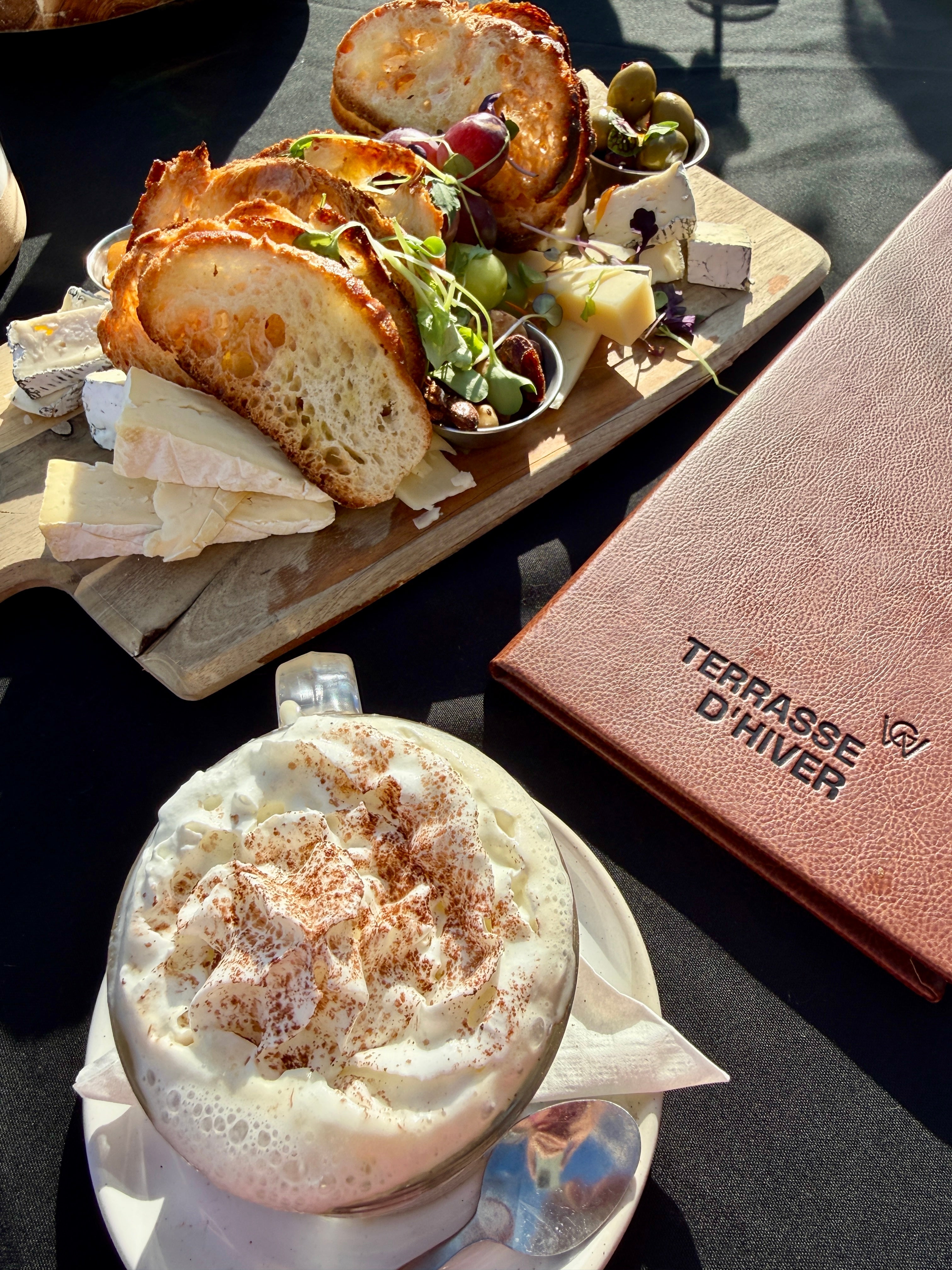 Gourmet food and breadstuff platter with a creamy drink, acceptable outdoors connected a sunny time with a paper titled "Terrasse D'Hiver" beside them