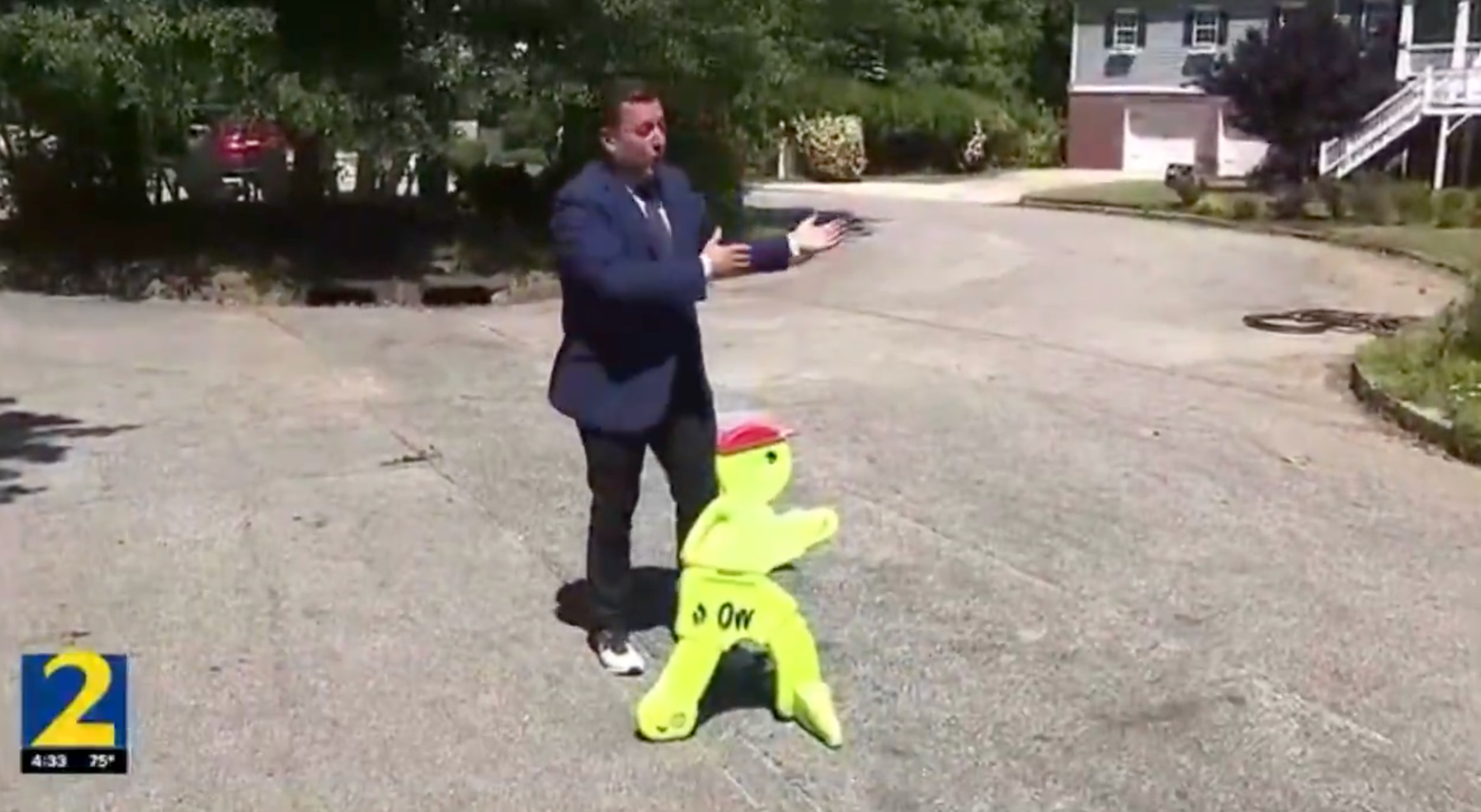 En mann gestikulerer humoristisk mens han står ved siden av en neongrønn forsiktighetsfigur i en forstadsgate, og formidler et lekent øyeblikk