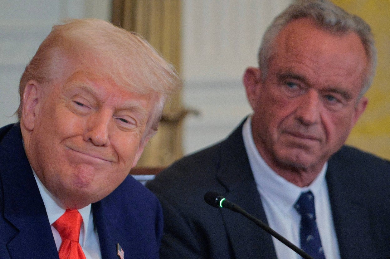 Two men in suits at a public event, seated next to each other, appear to be engaged in listening to a discussion