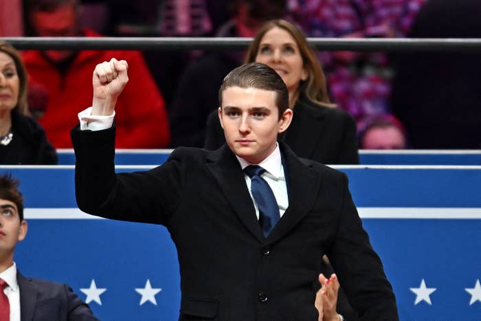 Person successful  a suit   raises a fist during an event, seated adjacent   others successful  an auditorium setting