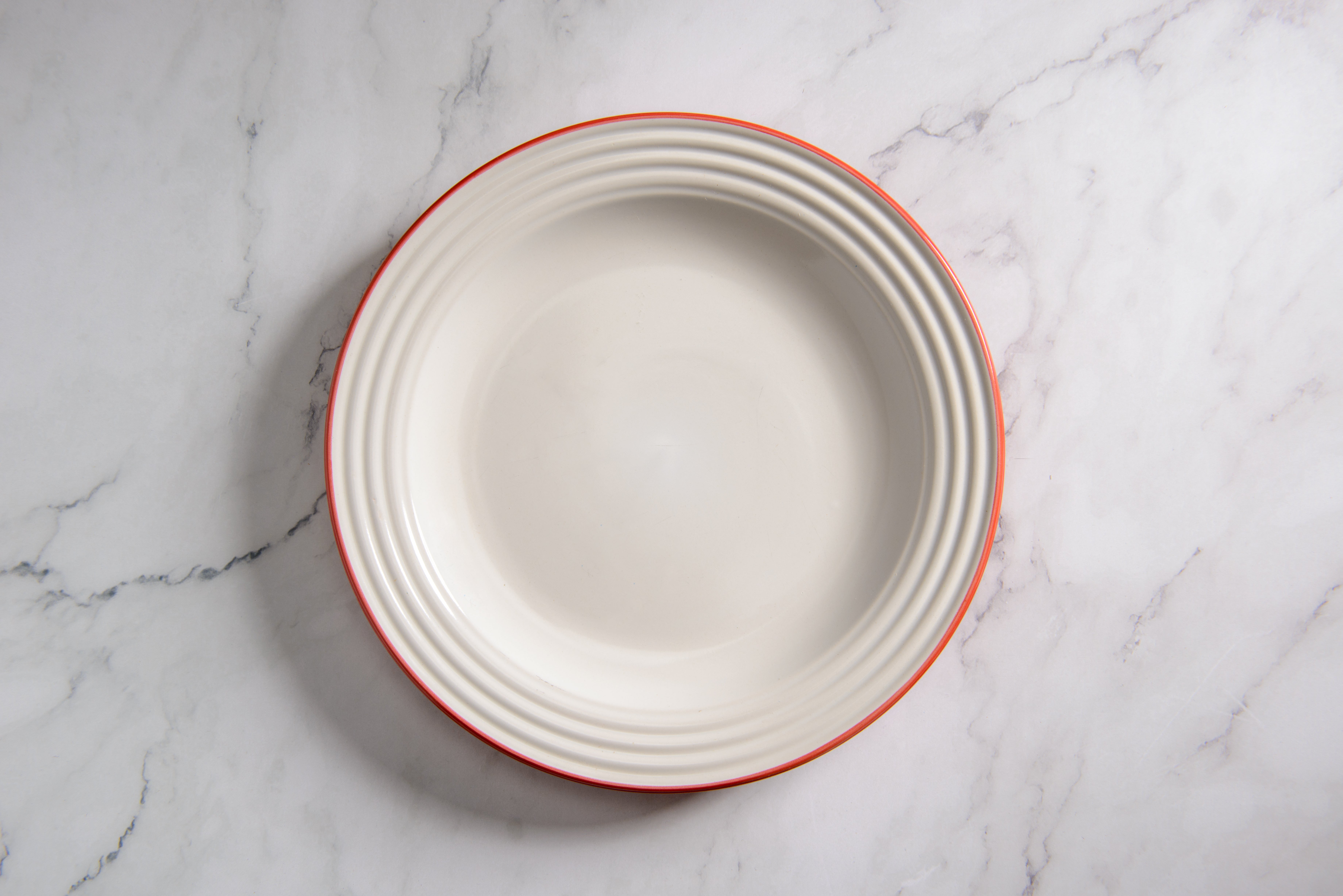 Empty round plate with ridged edges on a marble surface
