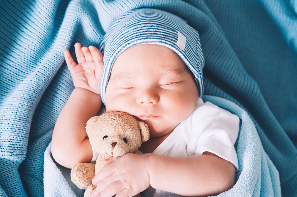 Sleeping baby in a striped hat cuddles a teddy bear, wrapped in a soft blanket