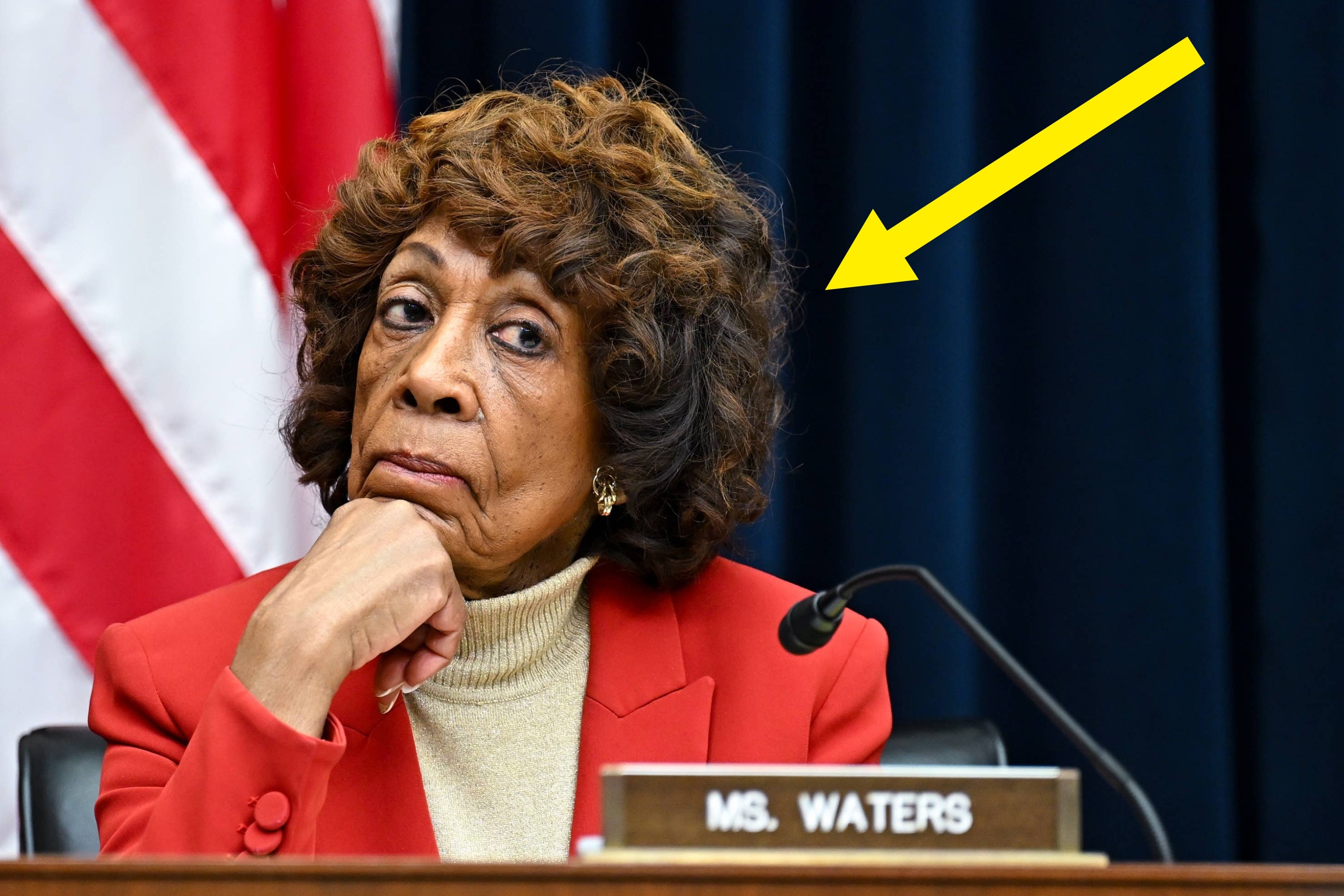 A person in a formal setting appears skeptical, wearing a turtleneck and blazer. A yellow arrow highlights their expression