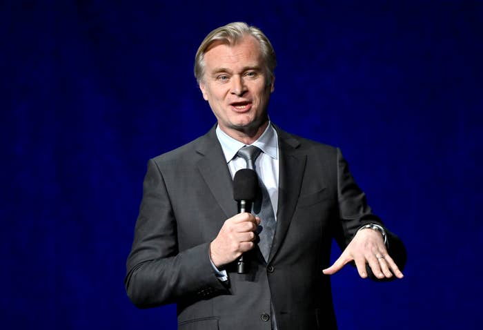 Man in a suit holding a microphone, speaking on stage