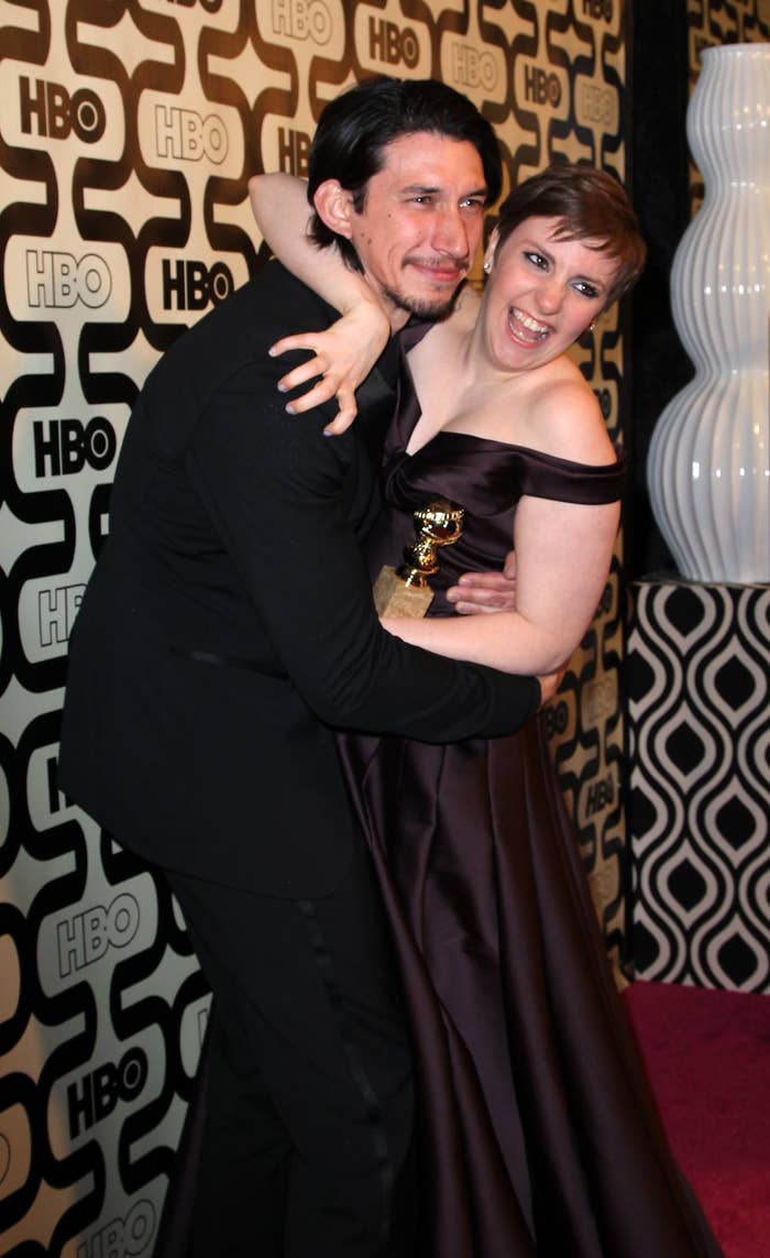 Two people hugging and smiling at an HBO event. One is holding an award and wearing an off-shoulder dress