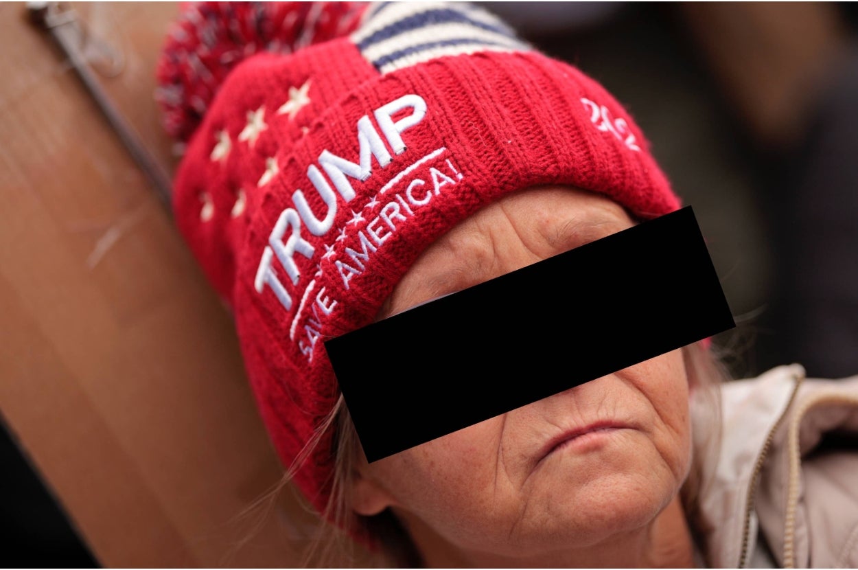Person wearing a knit hat with political text, face obscured. The hat has star details and a striped pom-pom