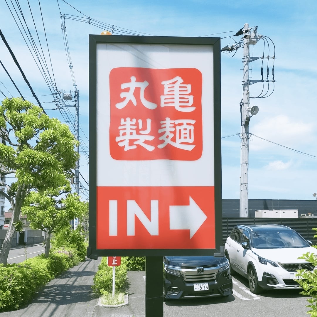看板に「丸亀製麺 IN」と書かれており、駐車場が見える。