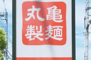 看板に「丸亀製麺 IN」と書かれており、駐車場が見える。
