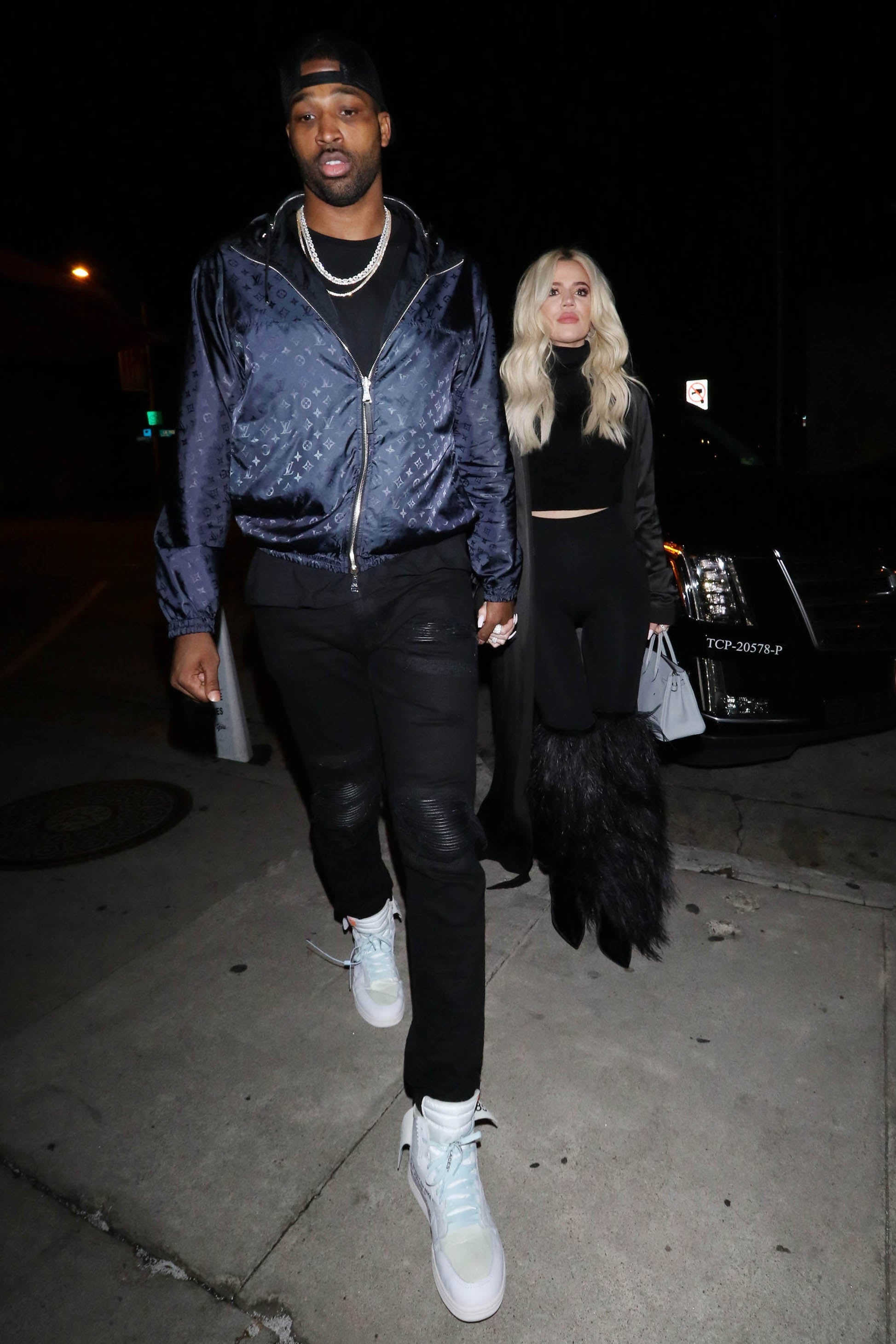 Tristan successful  casual overgarment   and pants holds hands with Khloe successful  achromatic  outfit adorned with fur accents, walking extracurricular  astatine  night
