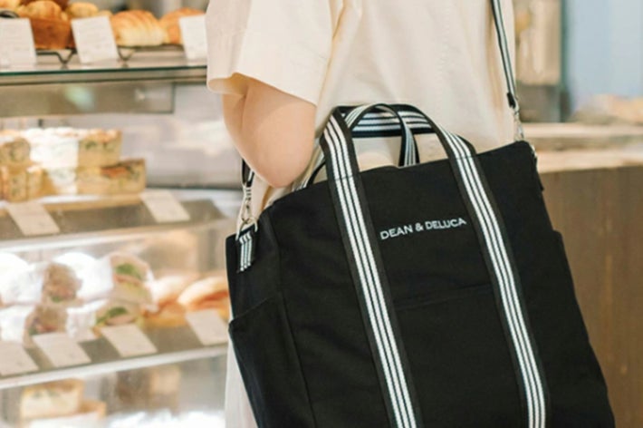 DEAN & DELUCAのロゴが入ったトートバッグを持つ人が、ベーカリーカウンターの前に立っている。