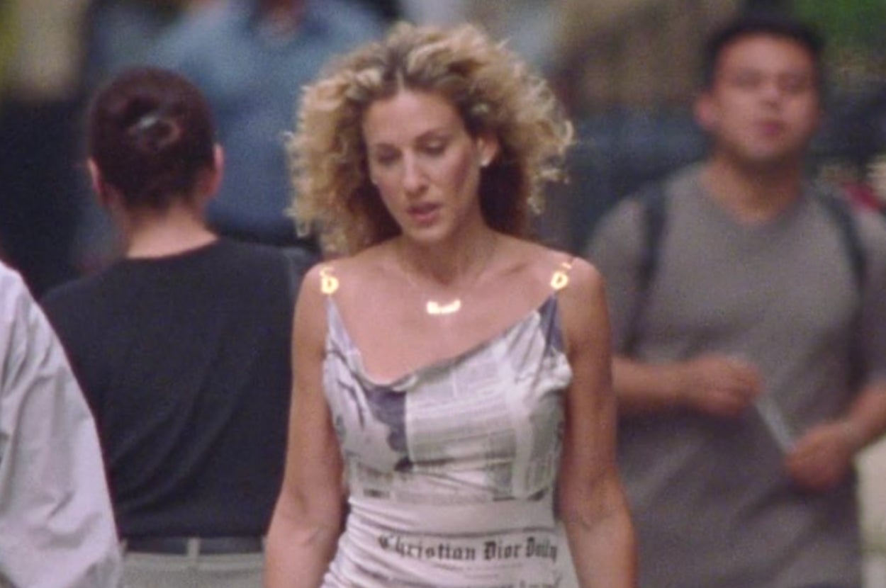 Person walking on a city street wearing a newspaper-print dress, styled with noticeable curly hair
