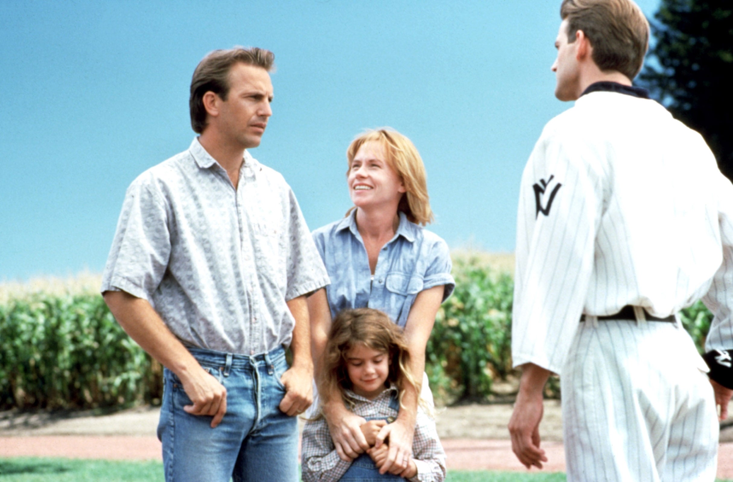 Four people stand in a field; two adults and a child interact with a man in a baseball uniform