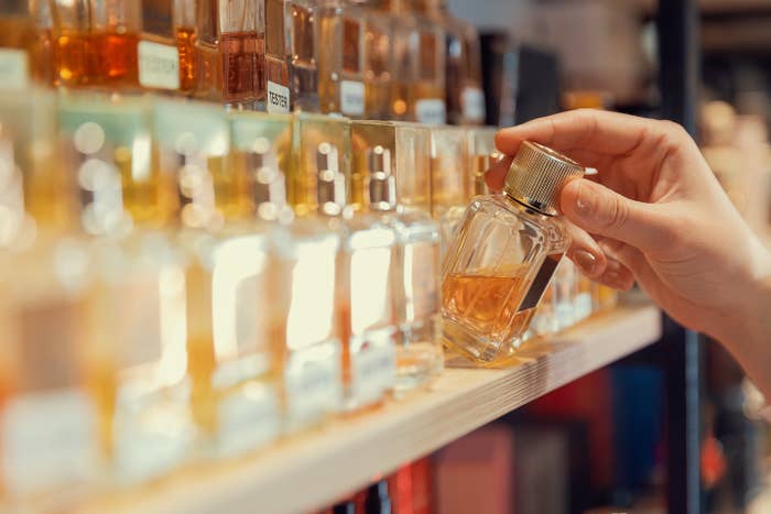 Person selecting a perfume vessel  from a store   shelf, surrounded by assorted  bottles