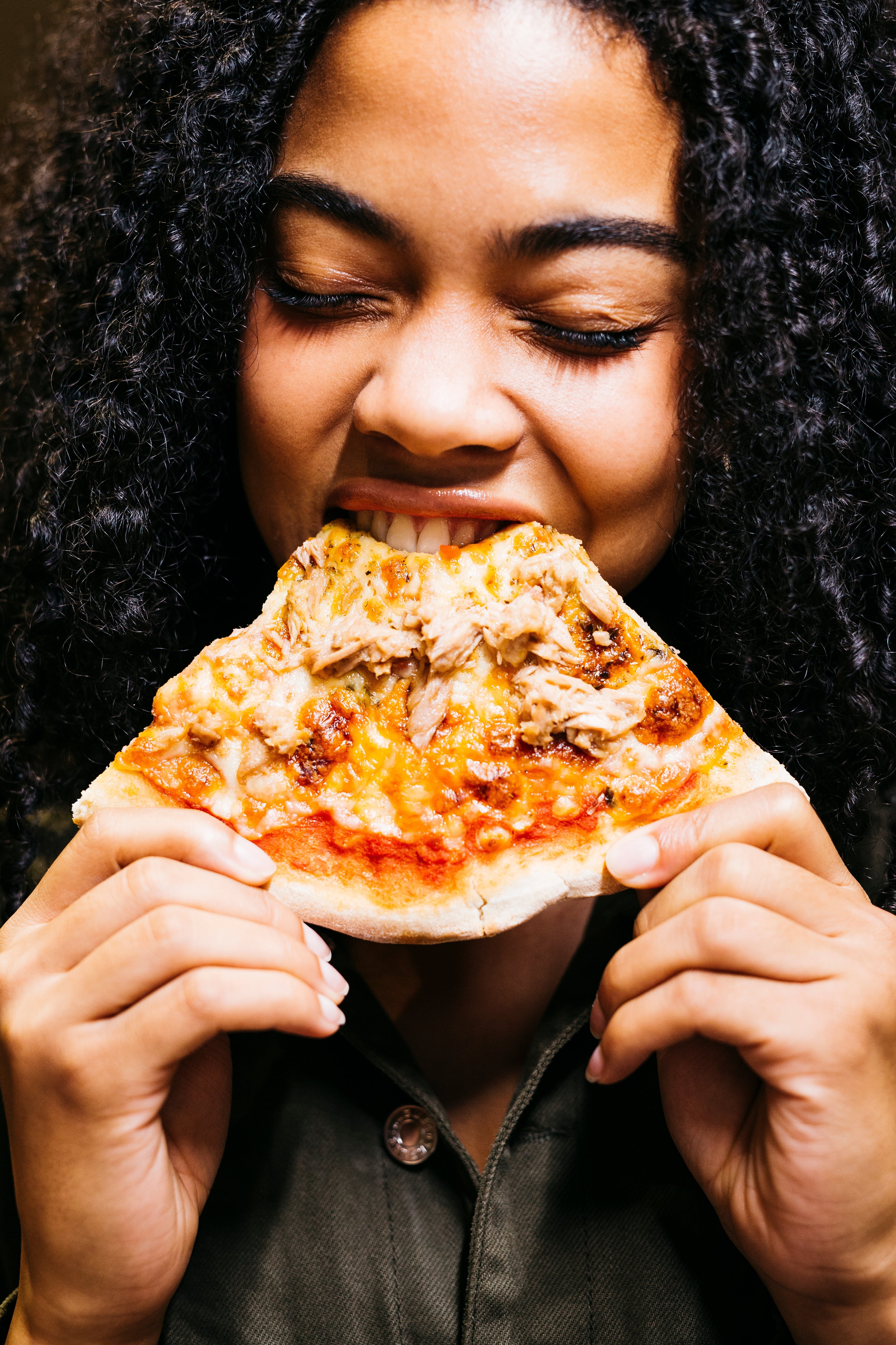 Person with curly hairsbreadth enjoying a portion of pizza, eyes closed successful delight