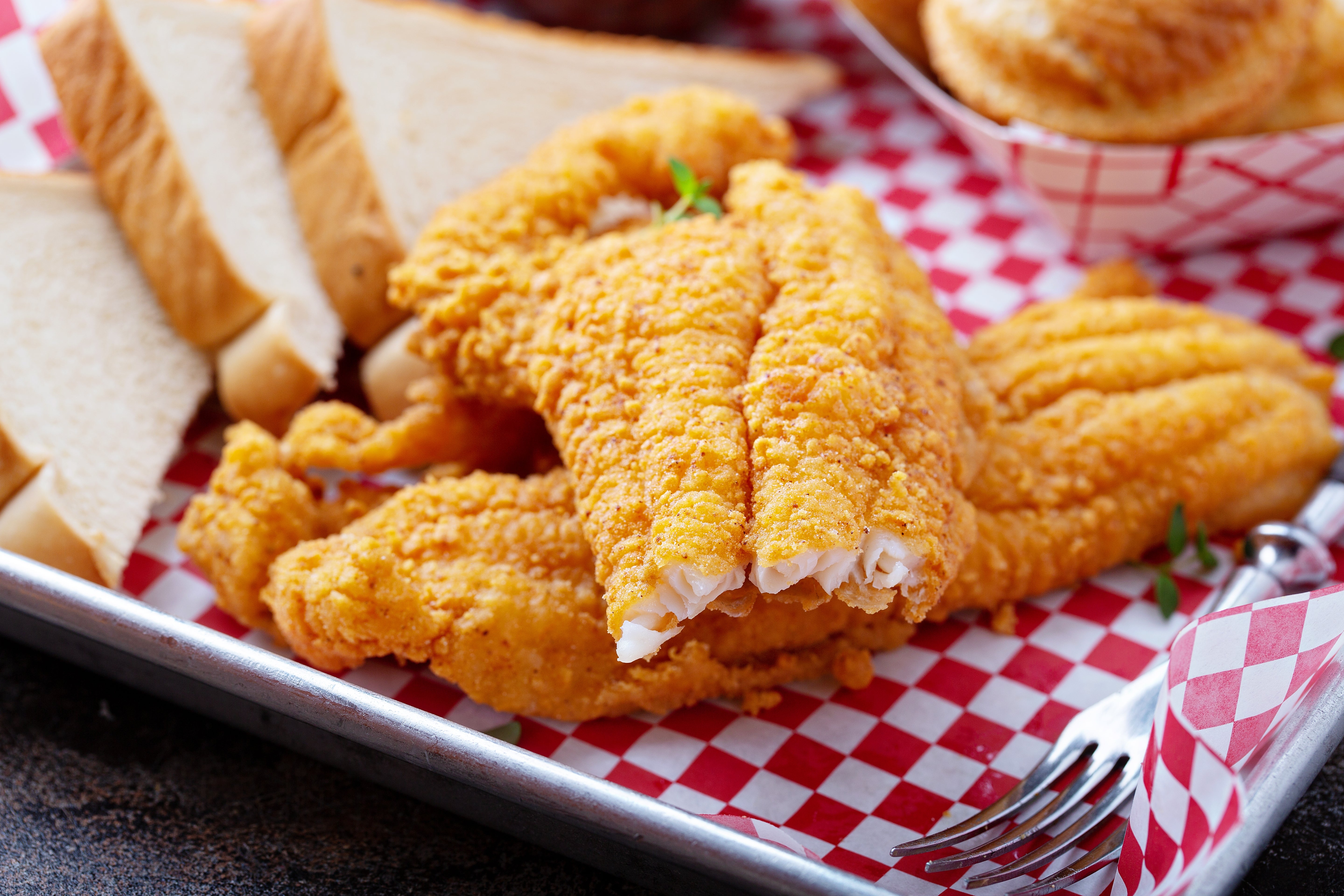 Fried food fillets and breadstuff slices arranged connected a reddish checkered tray, accompanied by a metallic fork