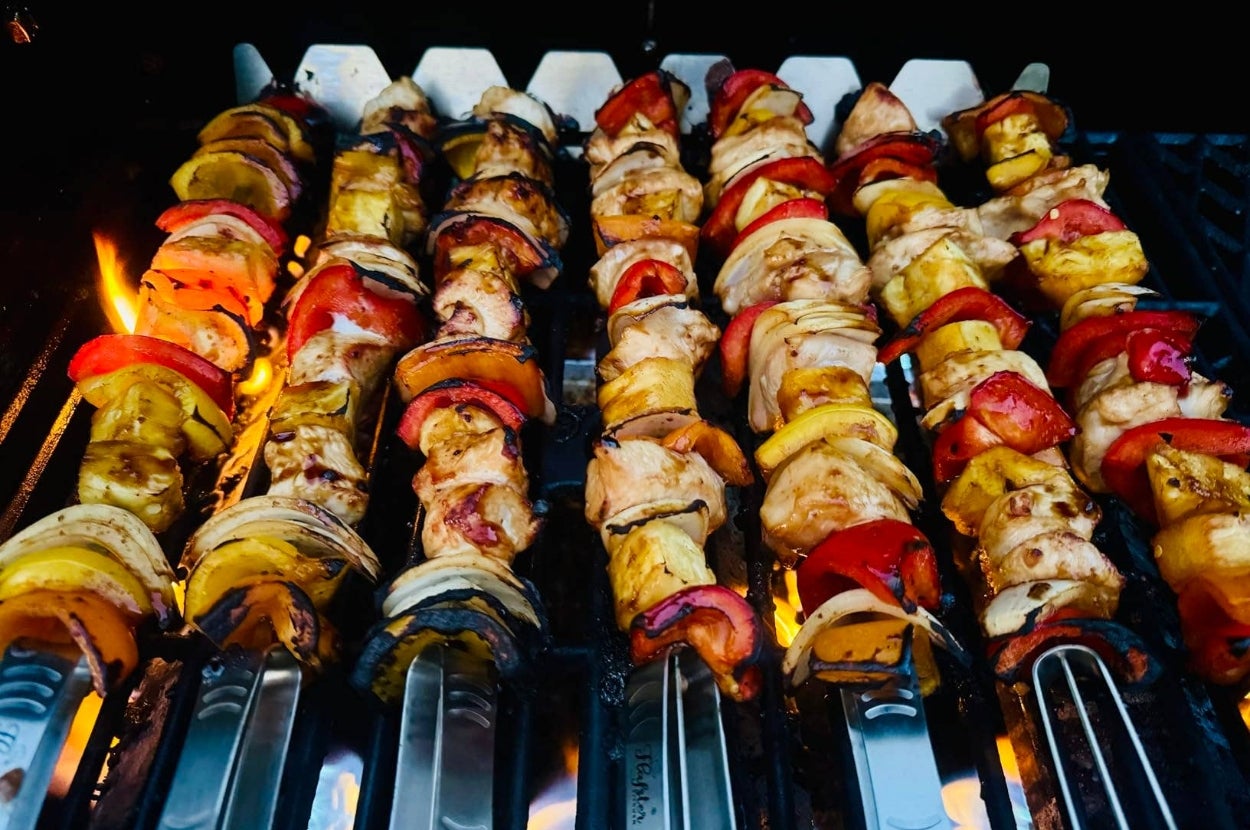 Skewers of grilled vegetables and meat cook on a barbecue grill, showcasing a delicious outdoor cooking option perfect for summer meals
