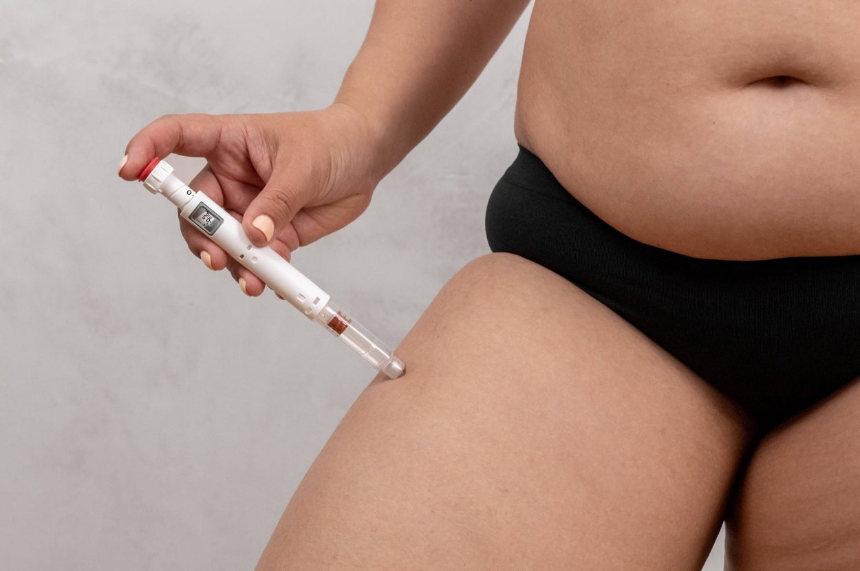 A person administers an injection into their thigh with an insulin pen, highlighting diabetes management and health care