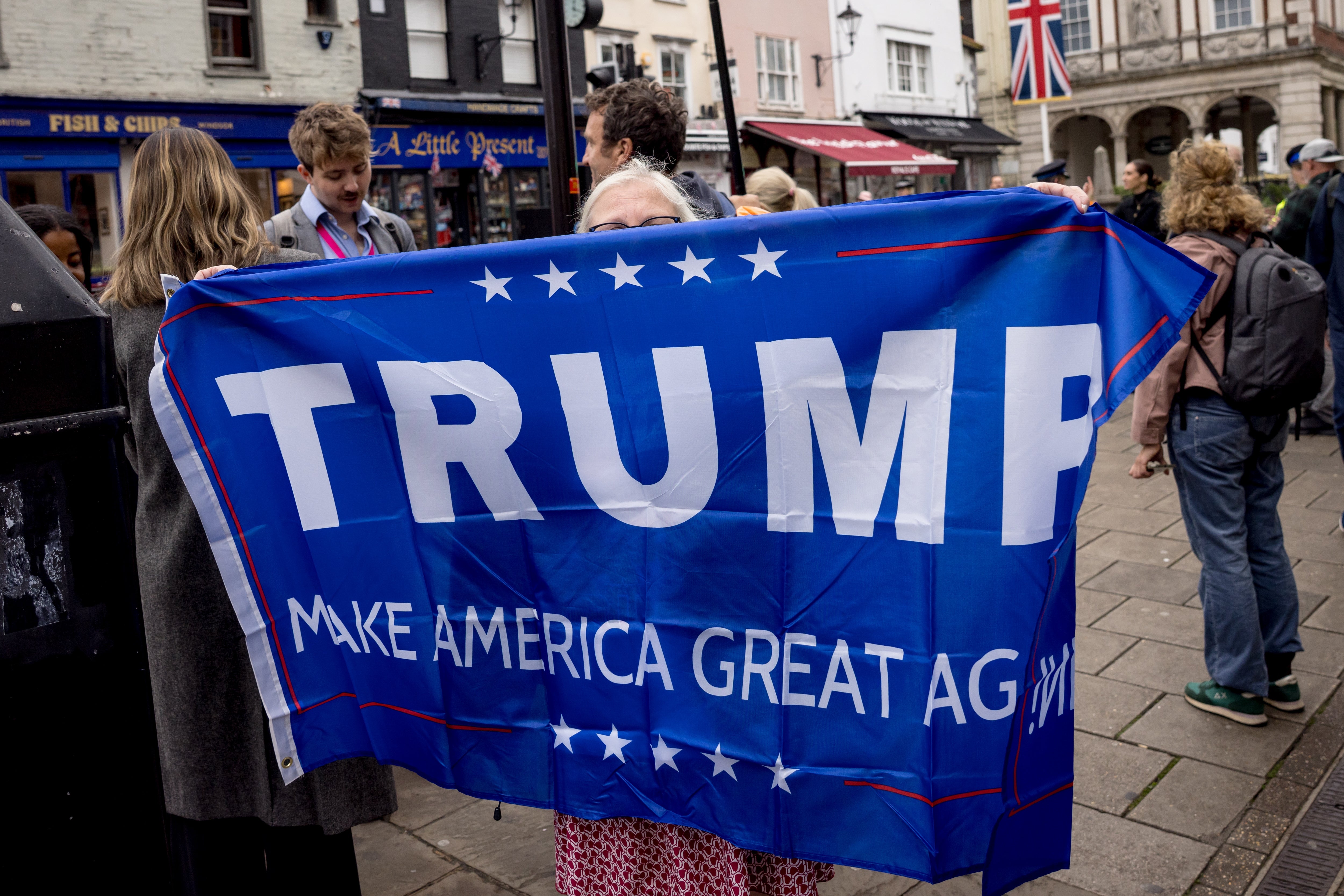 Individuals displaying a "Trump Make America Great Again" banner in a public square