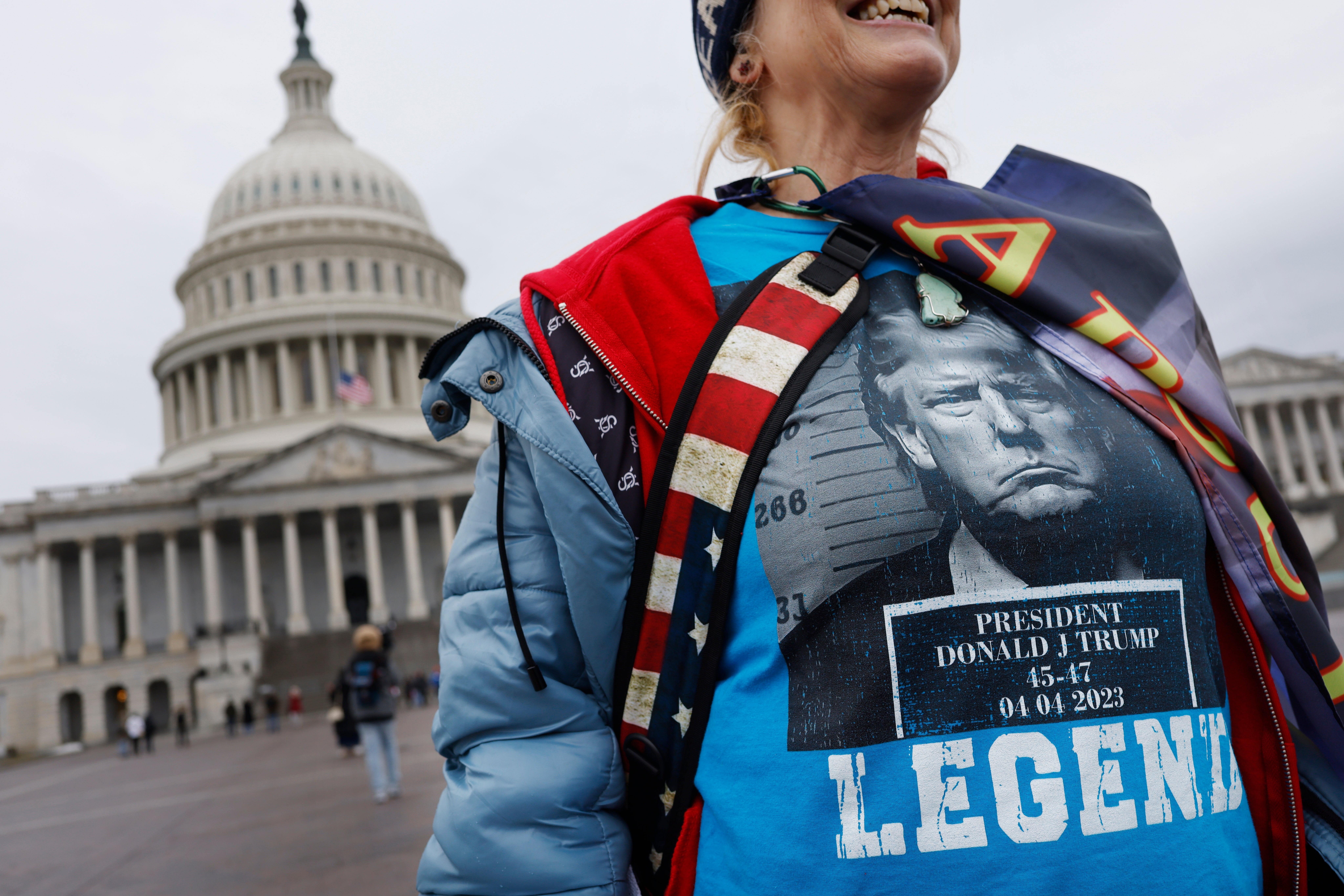 A person wearing a shirt with a graphic of Donald Trump and the word "Legend" stands in front of the U.S. Capitol