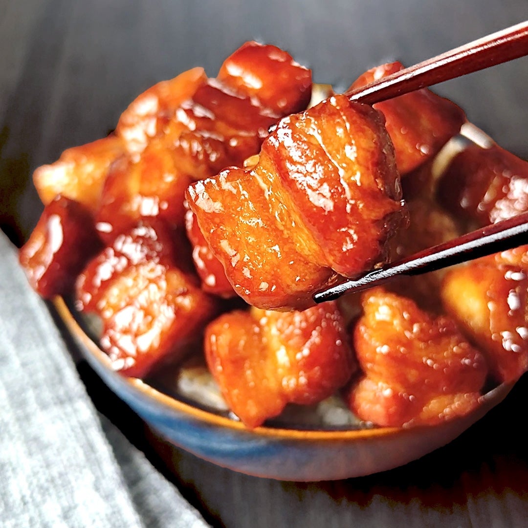 箸で持ち上げられた照り焼き風の肉。下に盛り付けられた同様の肉が見える。