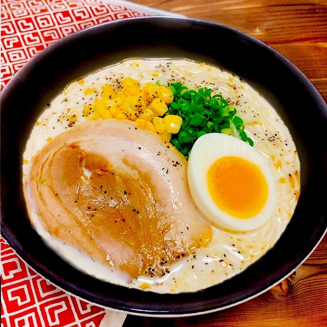 ラーメンの器にトウモロコシ、ねぎ、チャーシュー、ゆで卵がのった一杯がテーブルに置かれている。