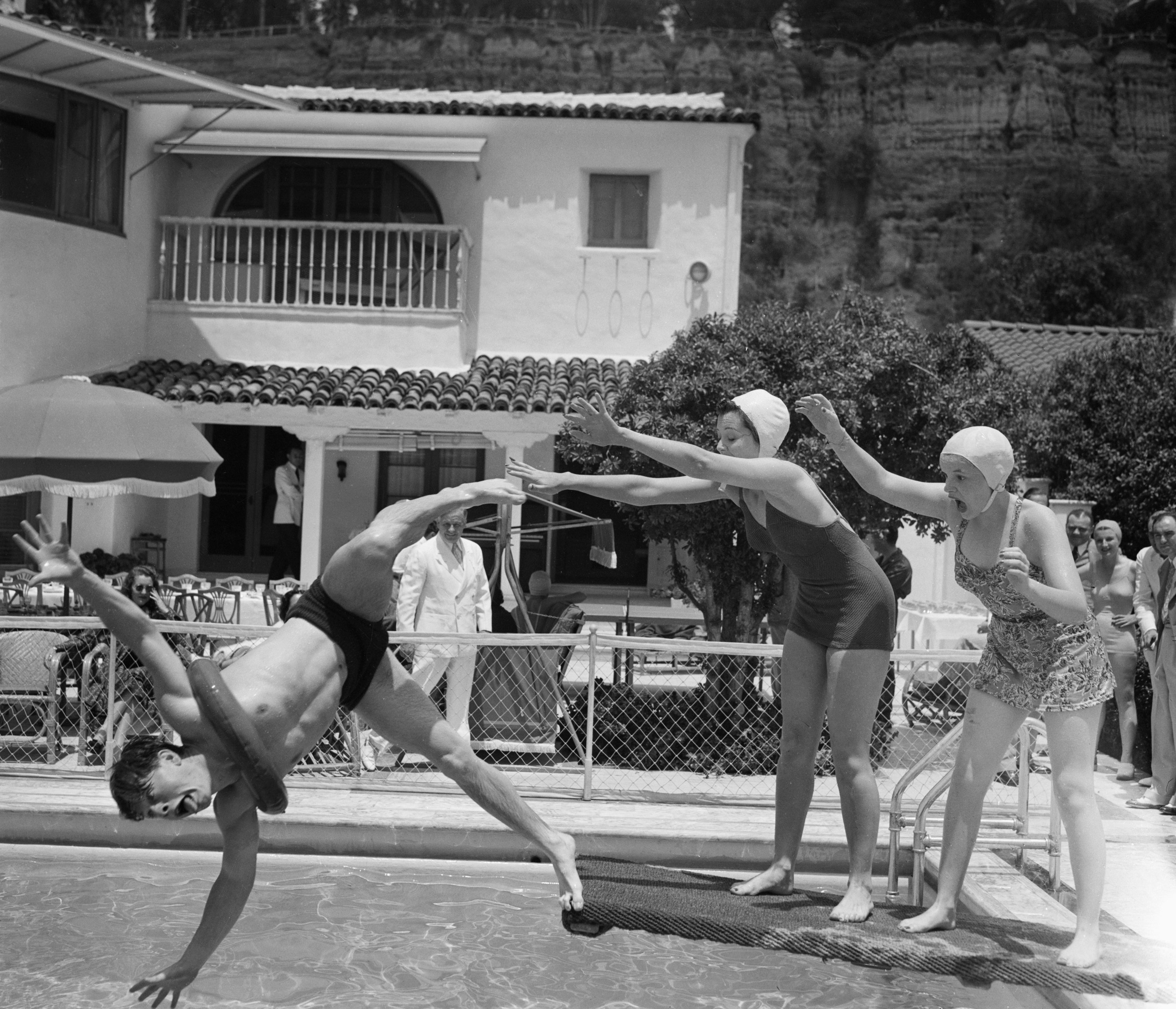 Mickey Rooney goofs off jumping into a pool while Ann Rutherford and Judy Garland reach out to him with surprised looks