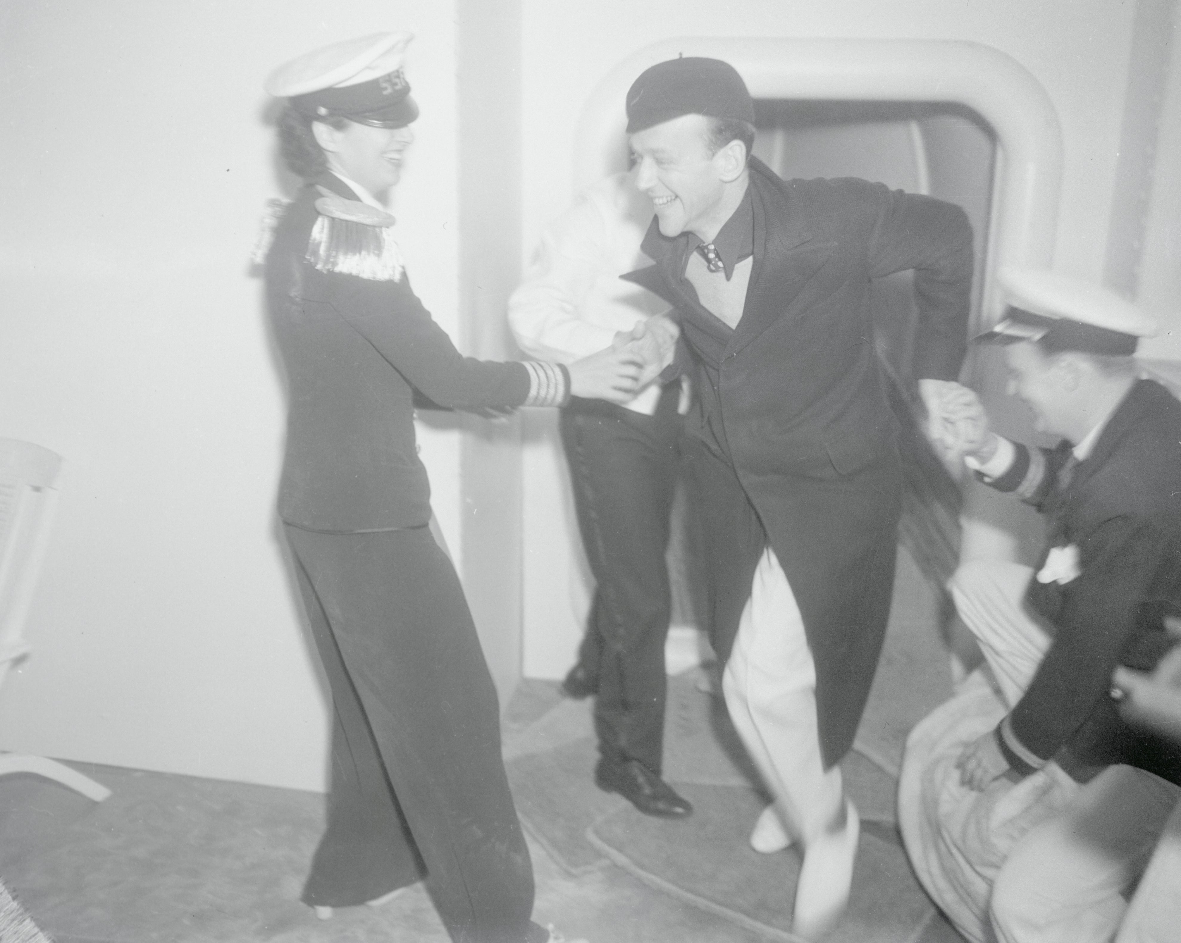 Kay Francis and Fred Astaire and others in naval-themed costumes laughing and dancing playfully in a room